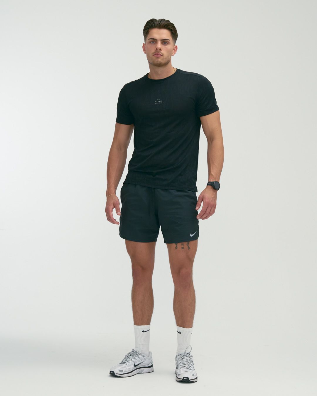 Person in black athletic attire and white sneakers demonstrates different standing poses against a white backdrop.
