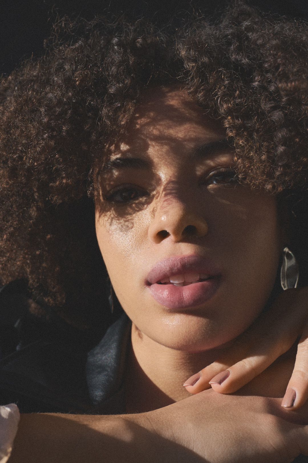 Close-up beauty shots highlighting natural curly hair and lips in dramatic lighting.
