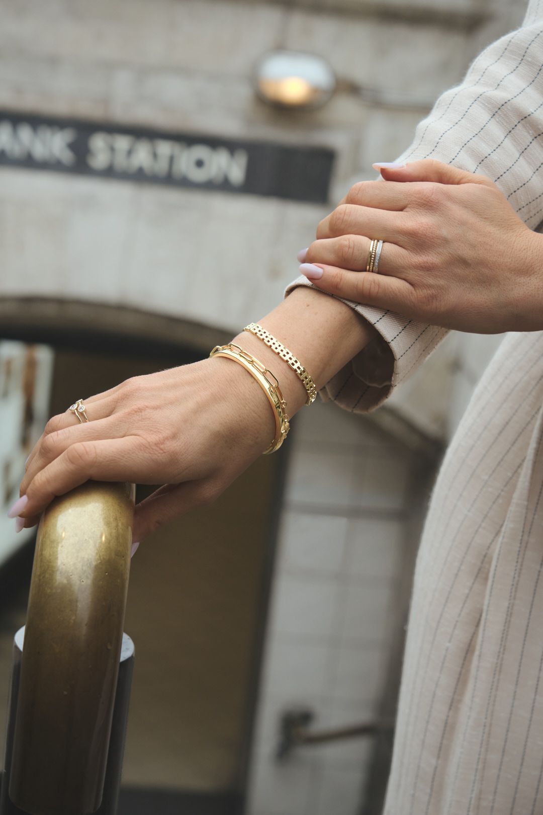 Close-up of hands wearing gold bracelets and rings against a light background.