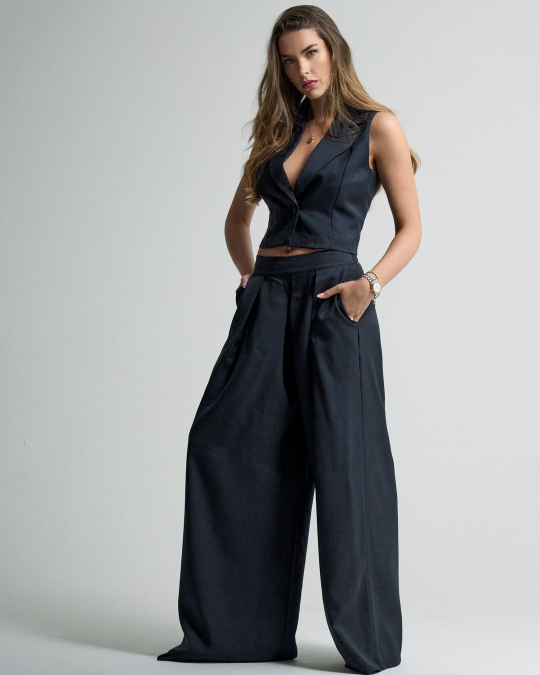 Model wearing a sleek black wide-leg jumpsuit with deep v-neck and tie waist detail against white background.