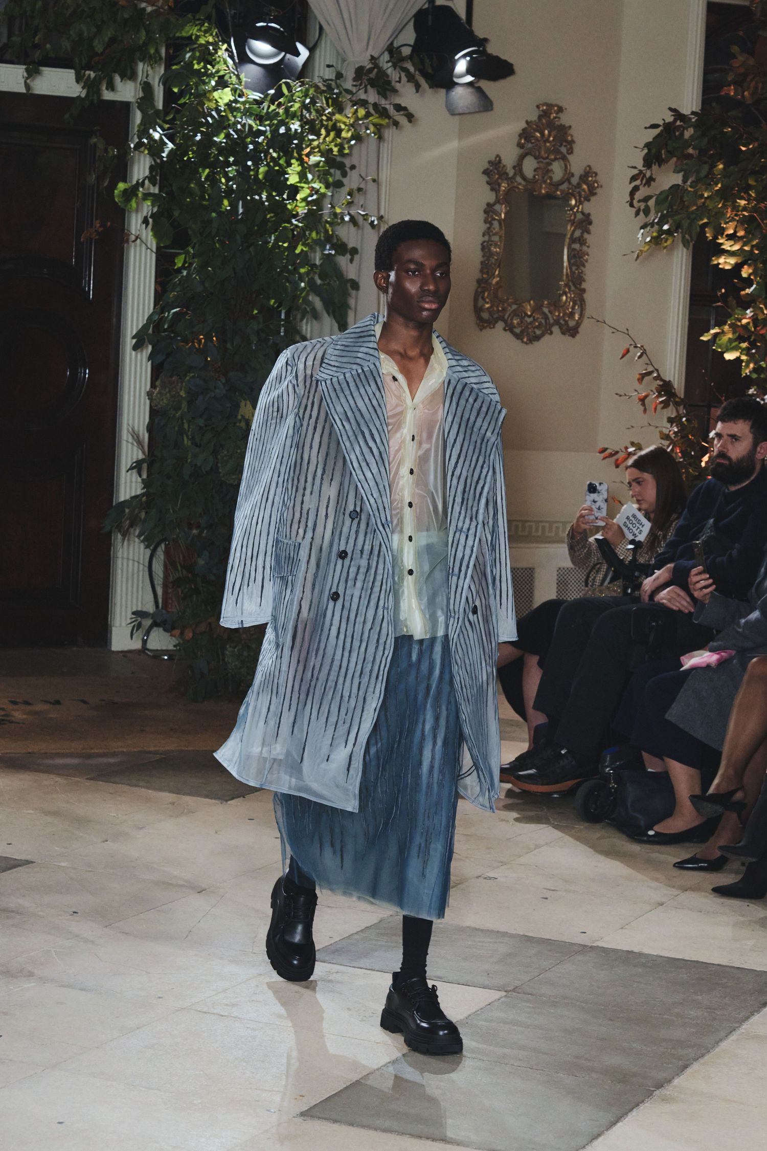 Model showcases gradient denim jacket with striped pattern on indoor fashion runway.