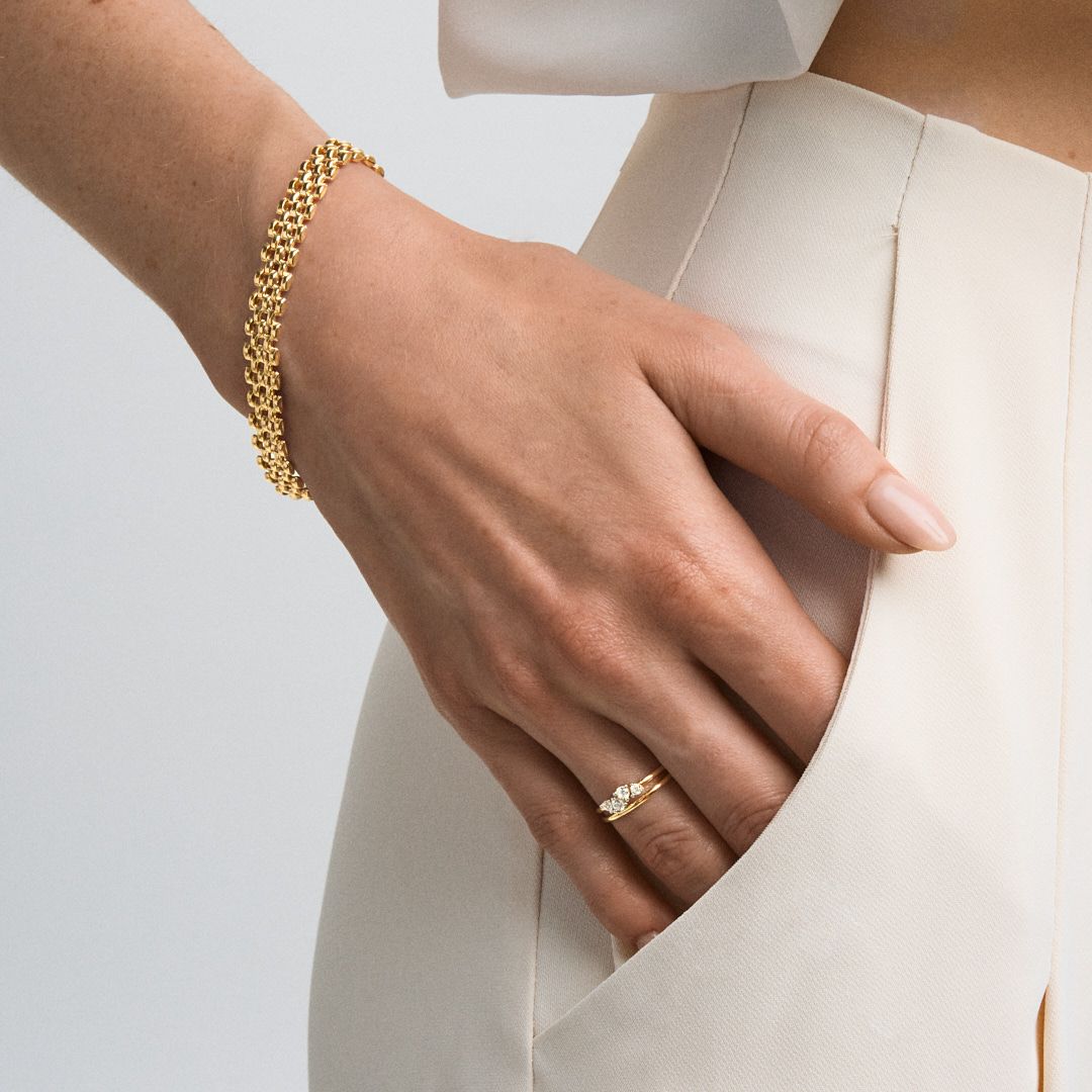 Woman wearing a gold chain bracelet and delicate diamond ring, styled with a cream blazer.