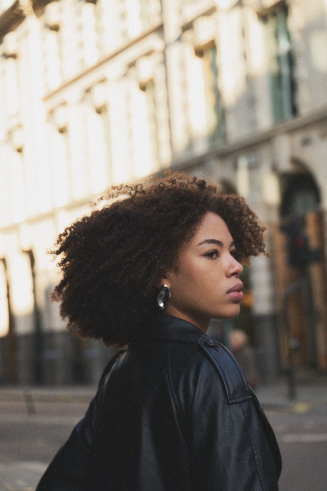 A fashion portrait series showing a person with natural curly hair in a black jacket against an urban backdrop.
