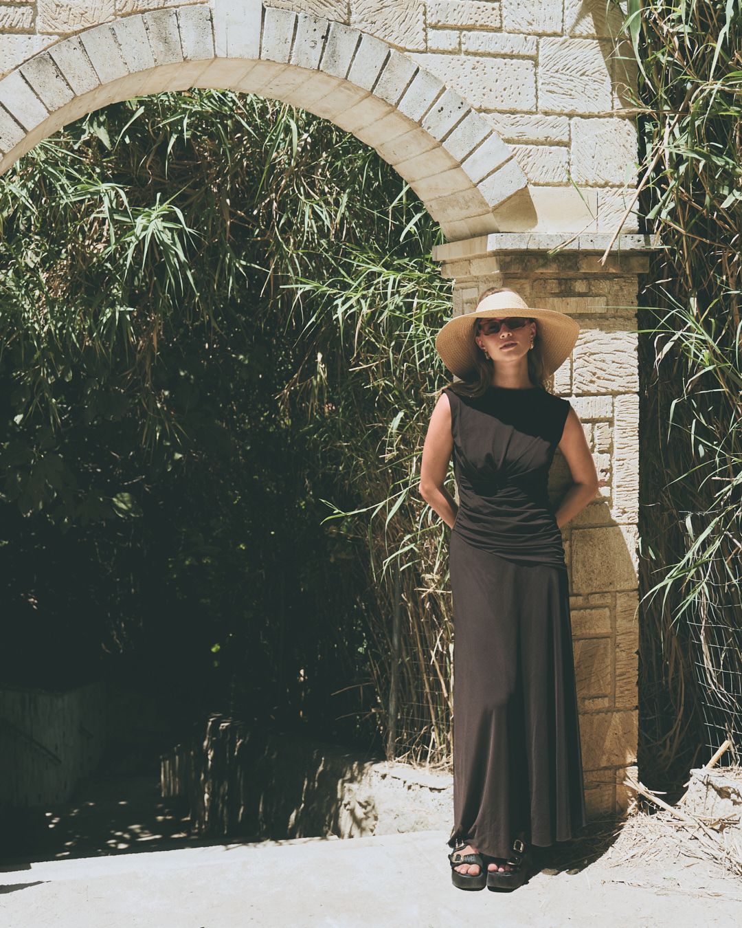 Four artful shots of someone in a brown dress posing beneath a stone archway in a garden setting.