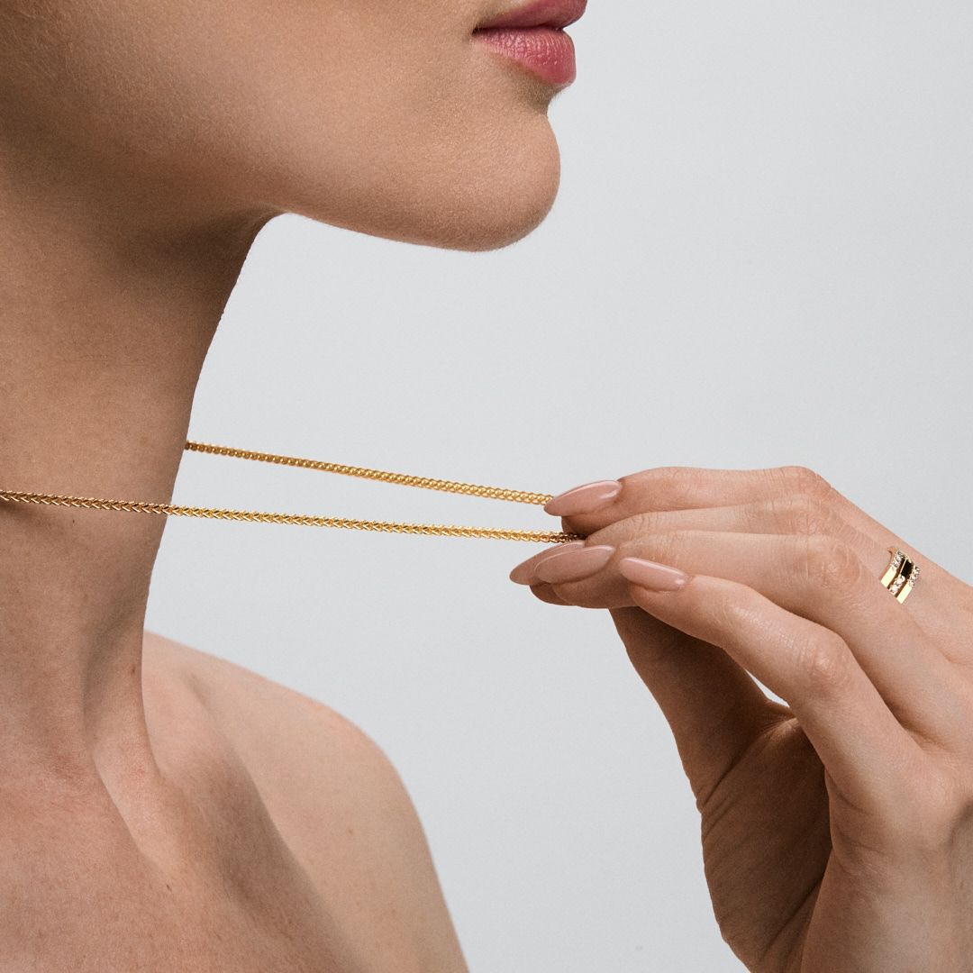 Woman wearing a delicate gold chain necklace and gold ring, gently holding the chain near her neck.