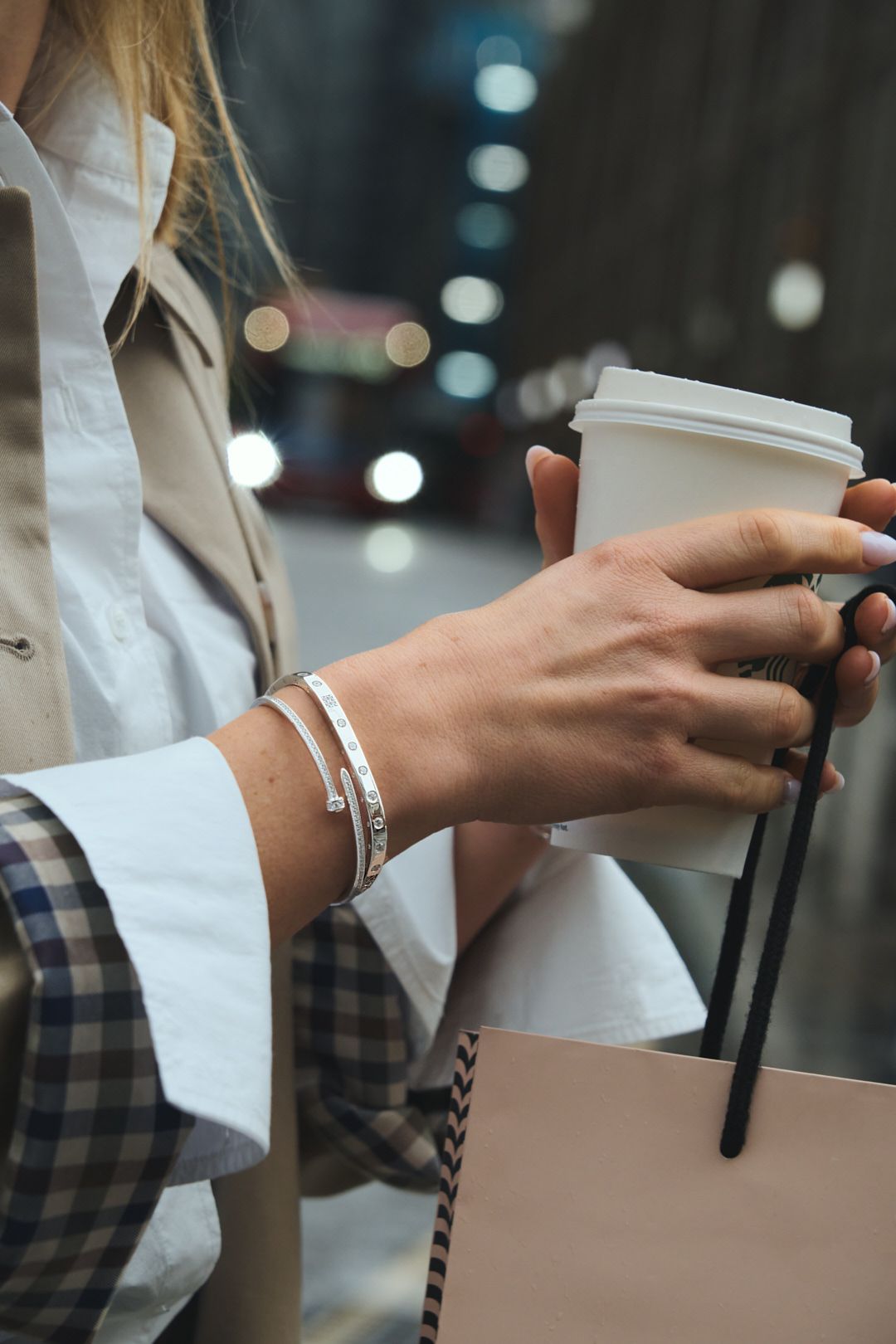 Hand wearing silver bracelet holding shopping bag with plaid and white sleeve details.