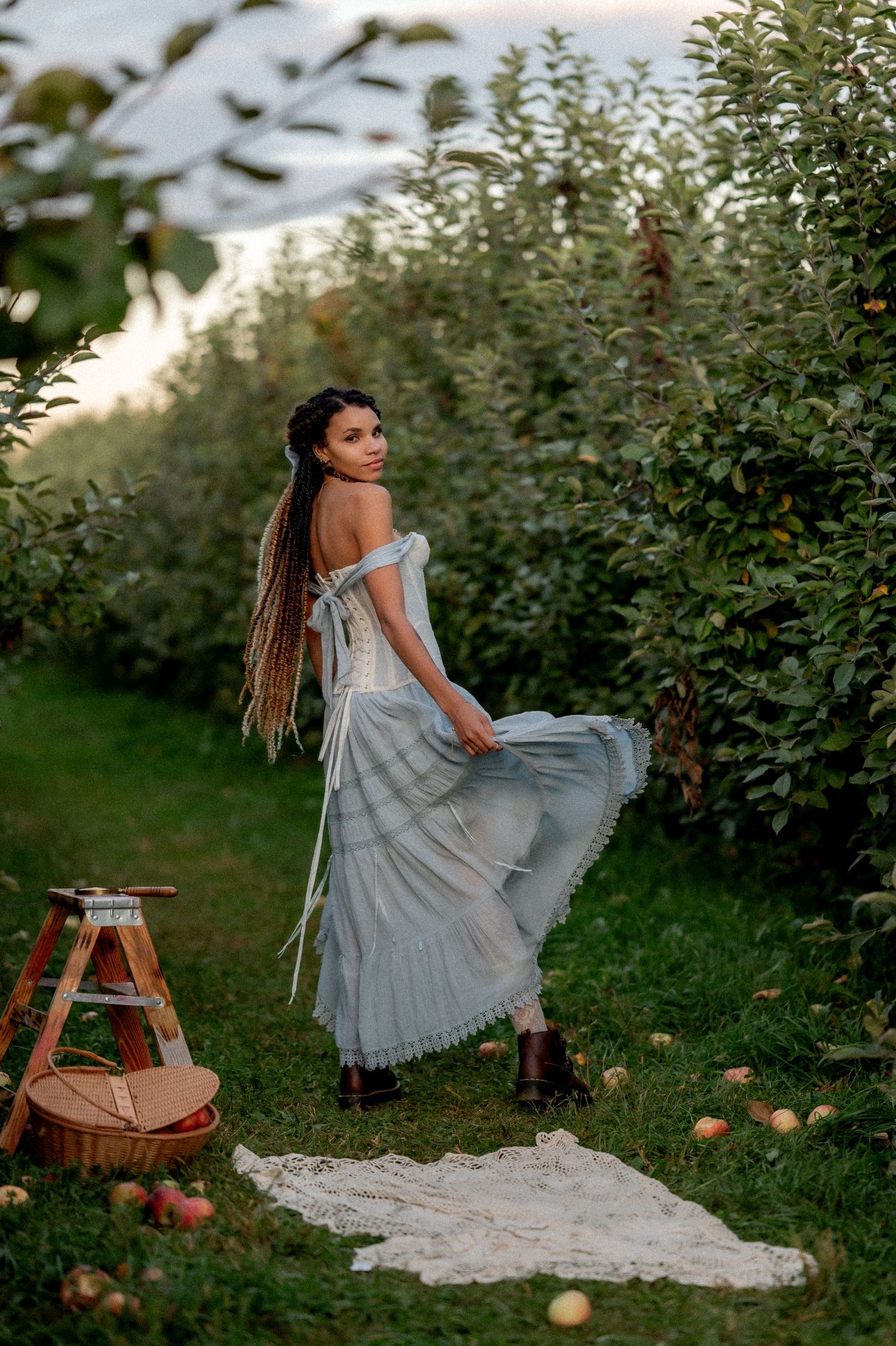 A dreamy portrait of a woman in a flowy dress posing in an apple orchard at golden hour.