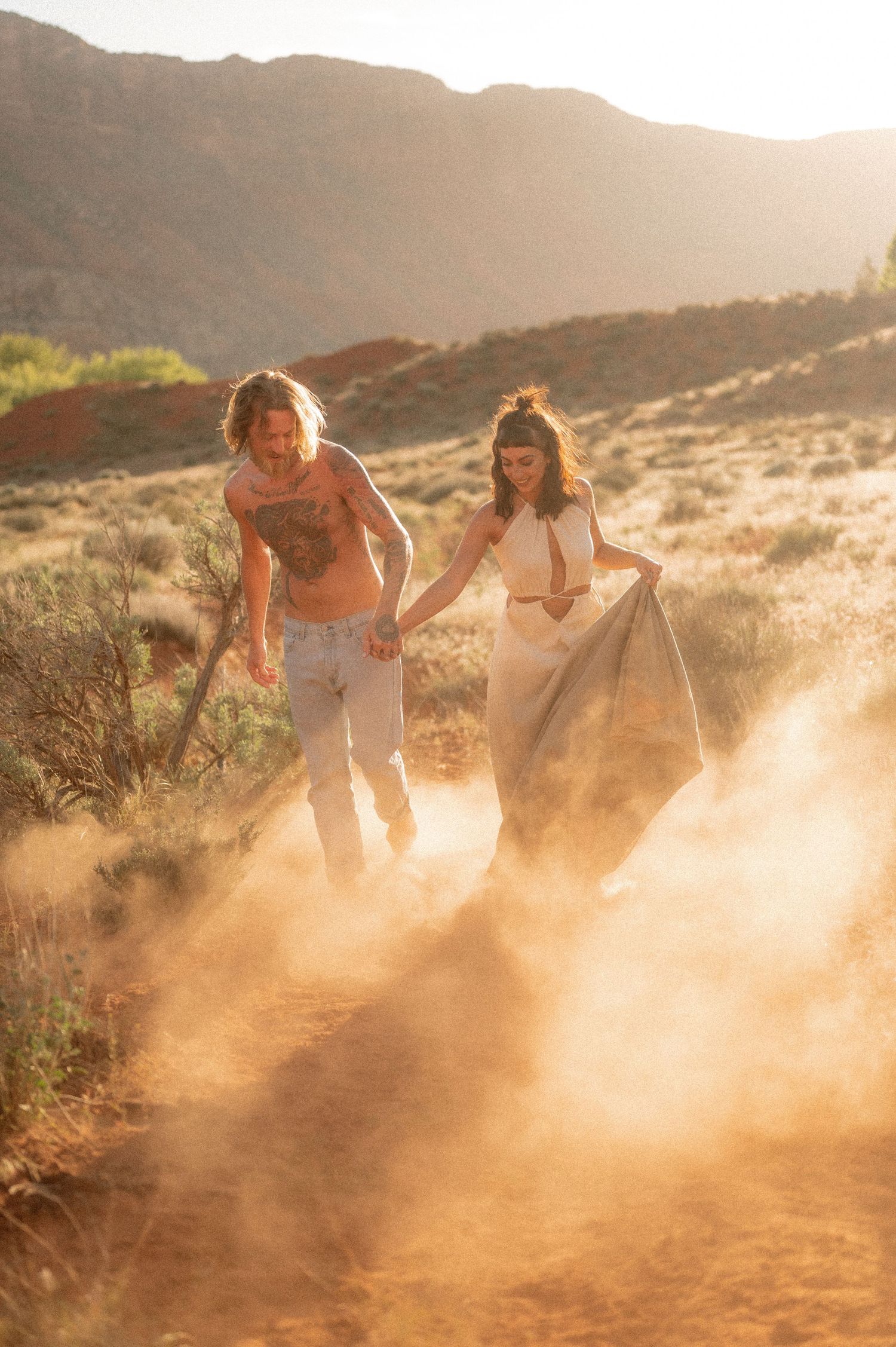Two people kick up dust while running along a mountain trail at golden hour.