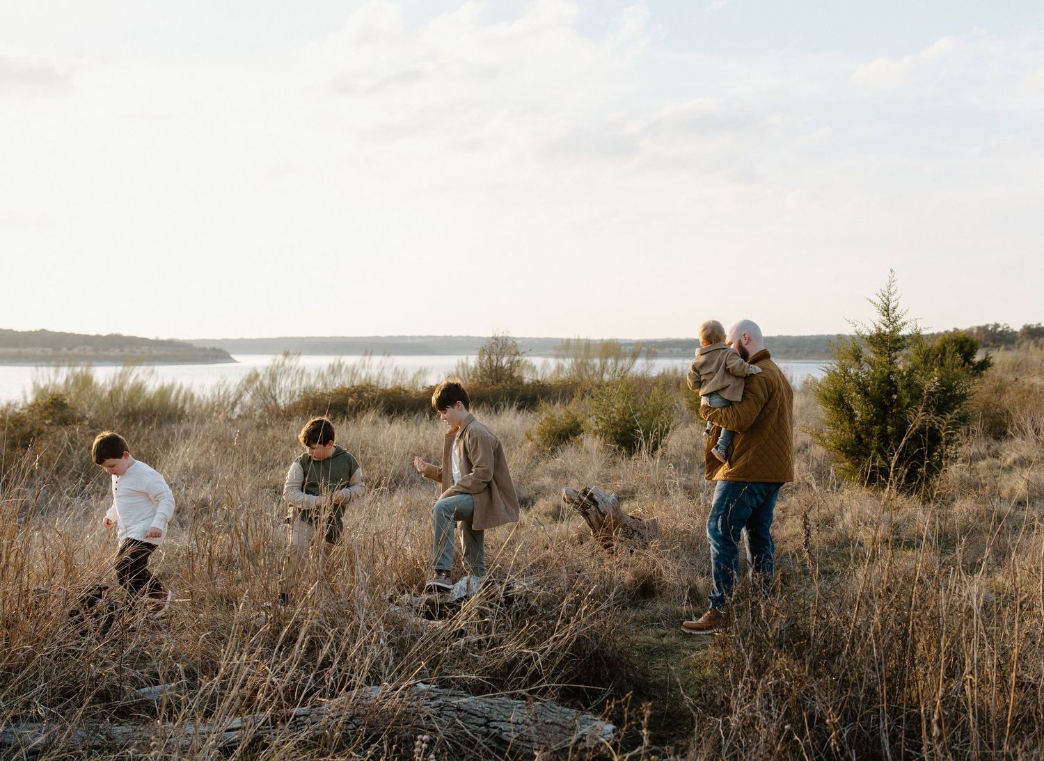 A family explores a rugged coastal trail together during golden hour at sunset overlooking the water.
