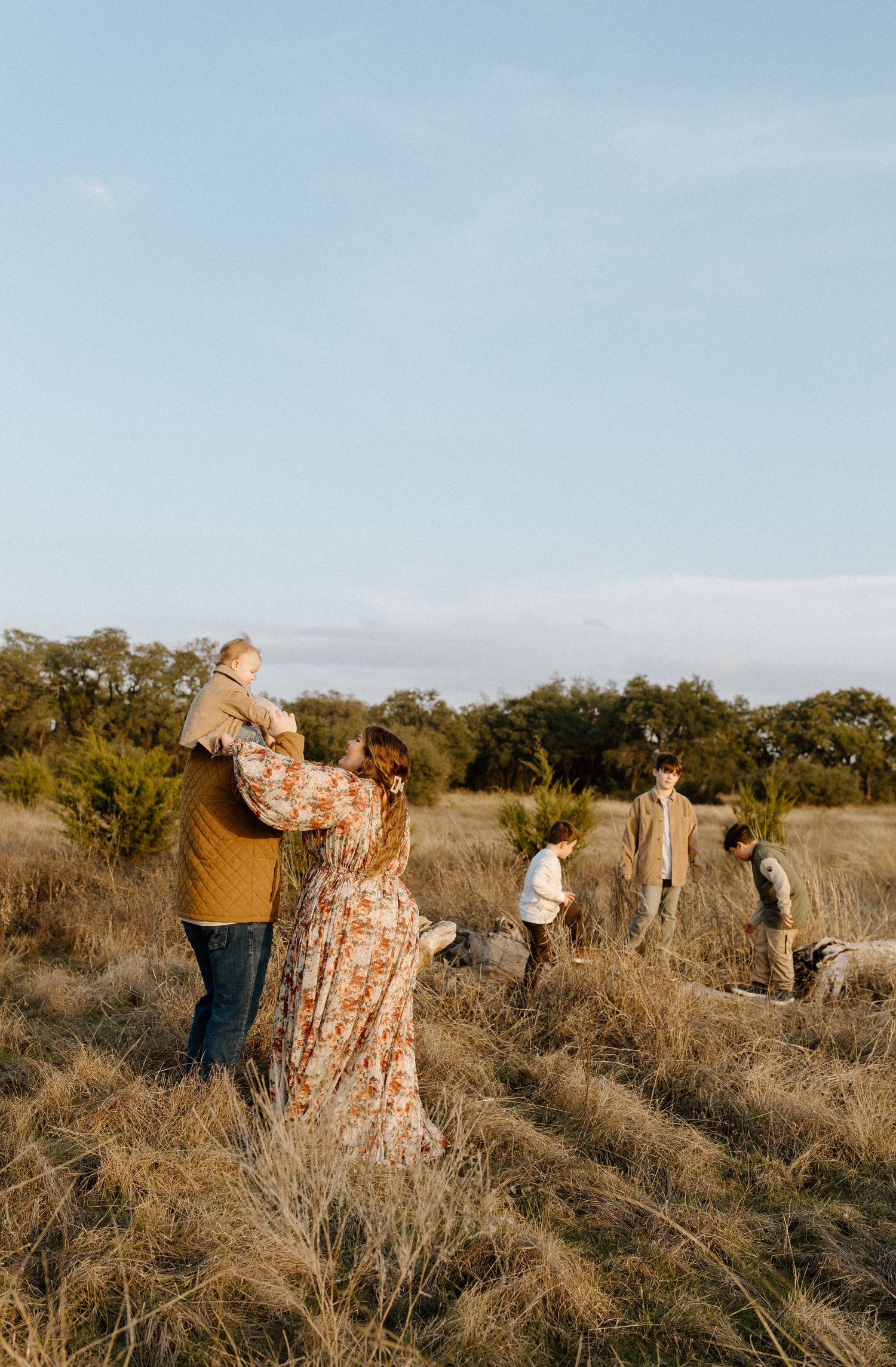 A couple dances in a field while others explore in the distance during sunset.