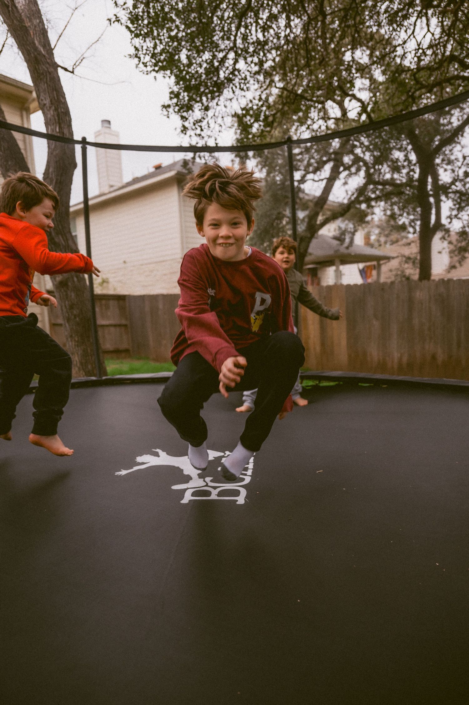 Children jumping and playing on a backyard trampoline on an overcast day.