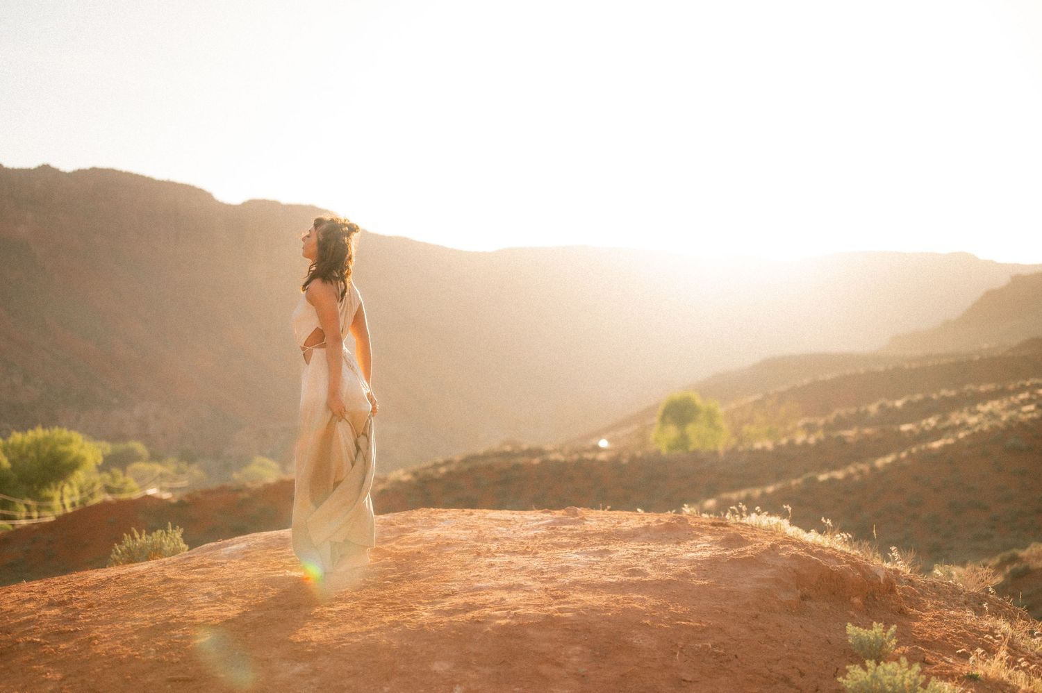 A figure stands on a rocky overlook against a mountainous desert landscape at sunset.