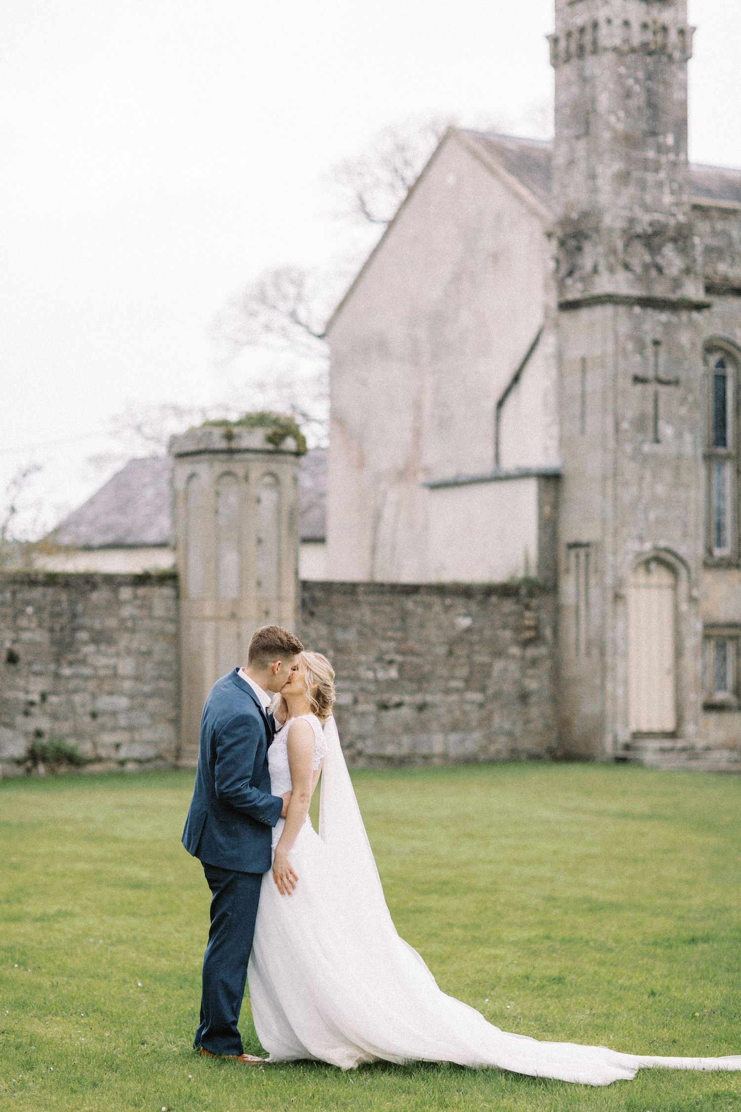 A newlywed couple shares a romantic moment on the lawn of a historic stone church in Ireland.