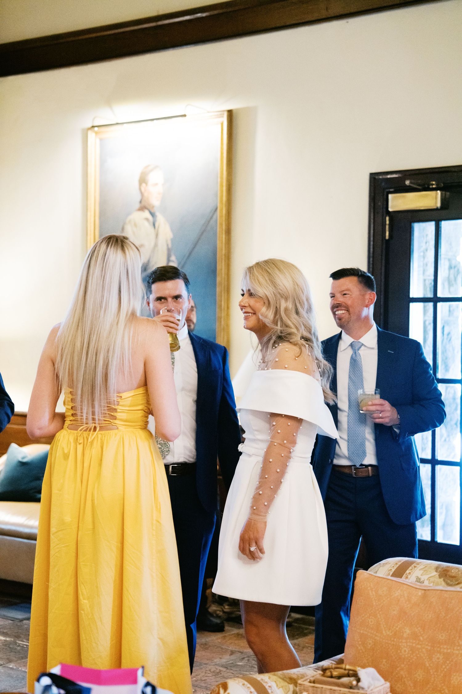 Party guests in formal attire socialize at an elegant indoor gathering with a yellow dress and white dress visible.