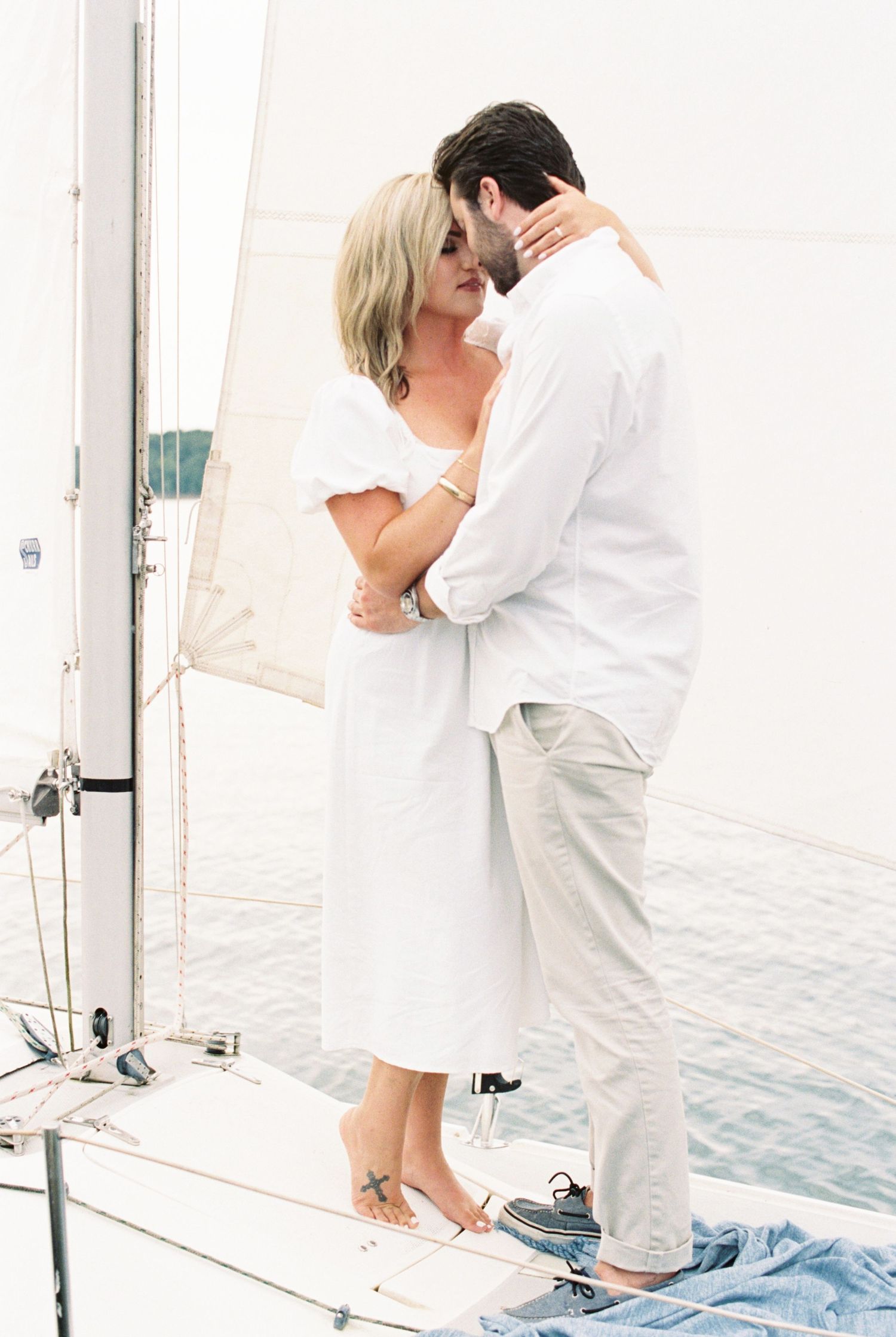 A romantic moment shared between a couple in white attire aboard a sailboat on the water.