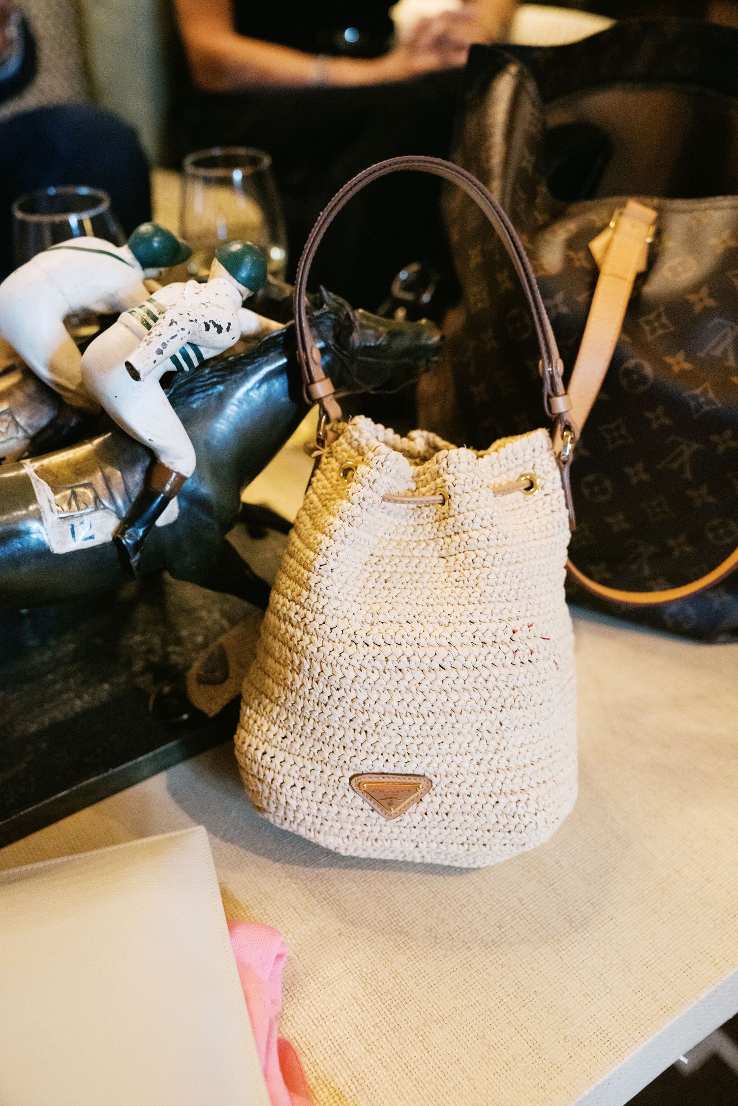 A cream-colored crochet bucket bag with leather handle sits on a table among shoes and accessories.