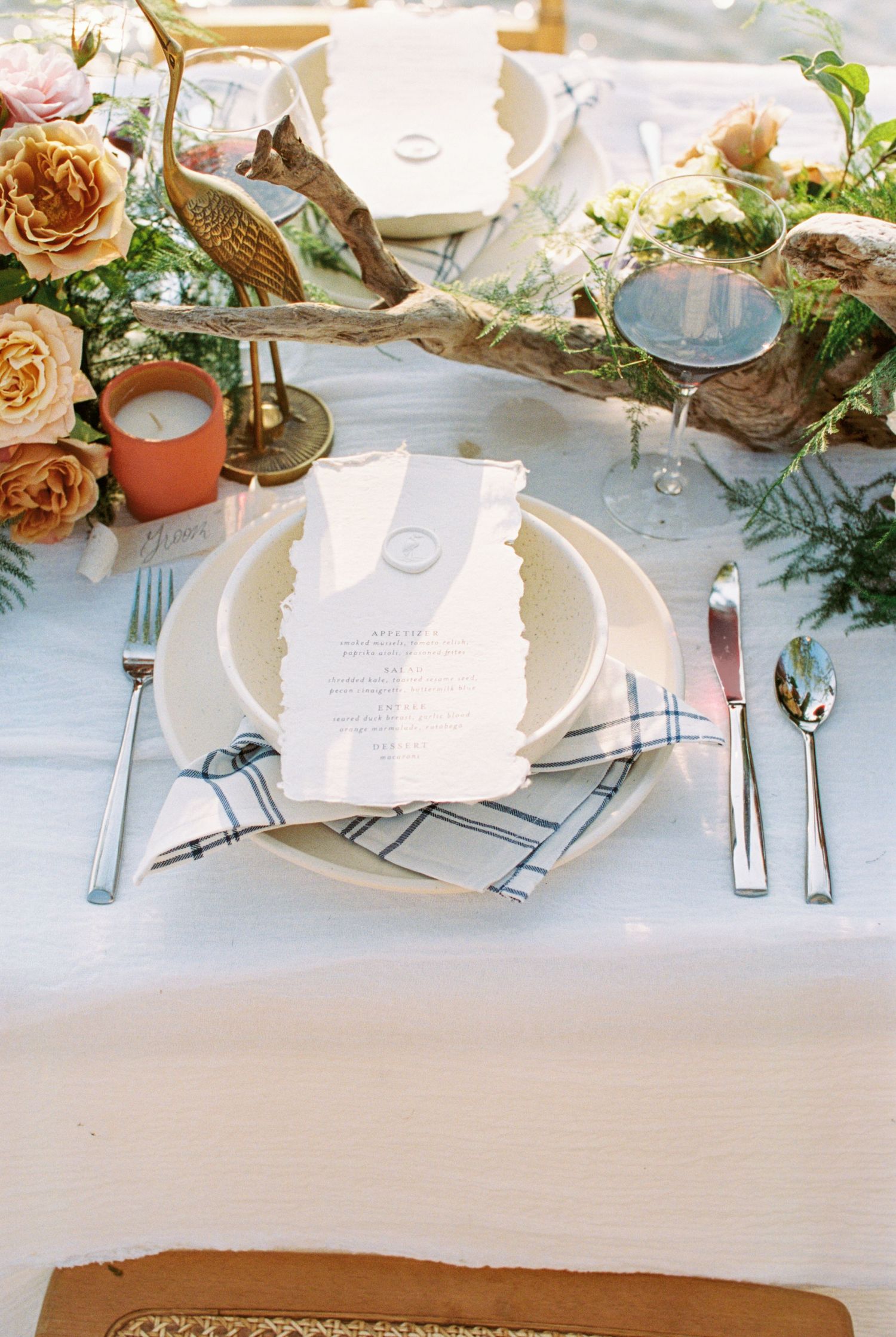 Elegant place setting with coral roses, gold accents, and torn-edge menu card on white linens. Kirstie Whitaker Photography