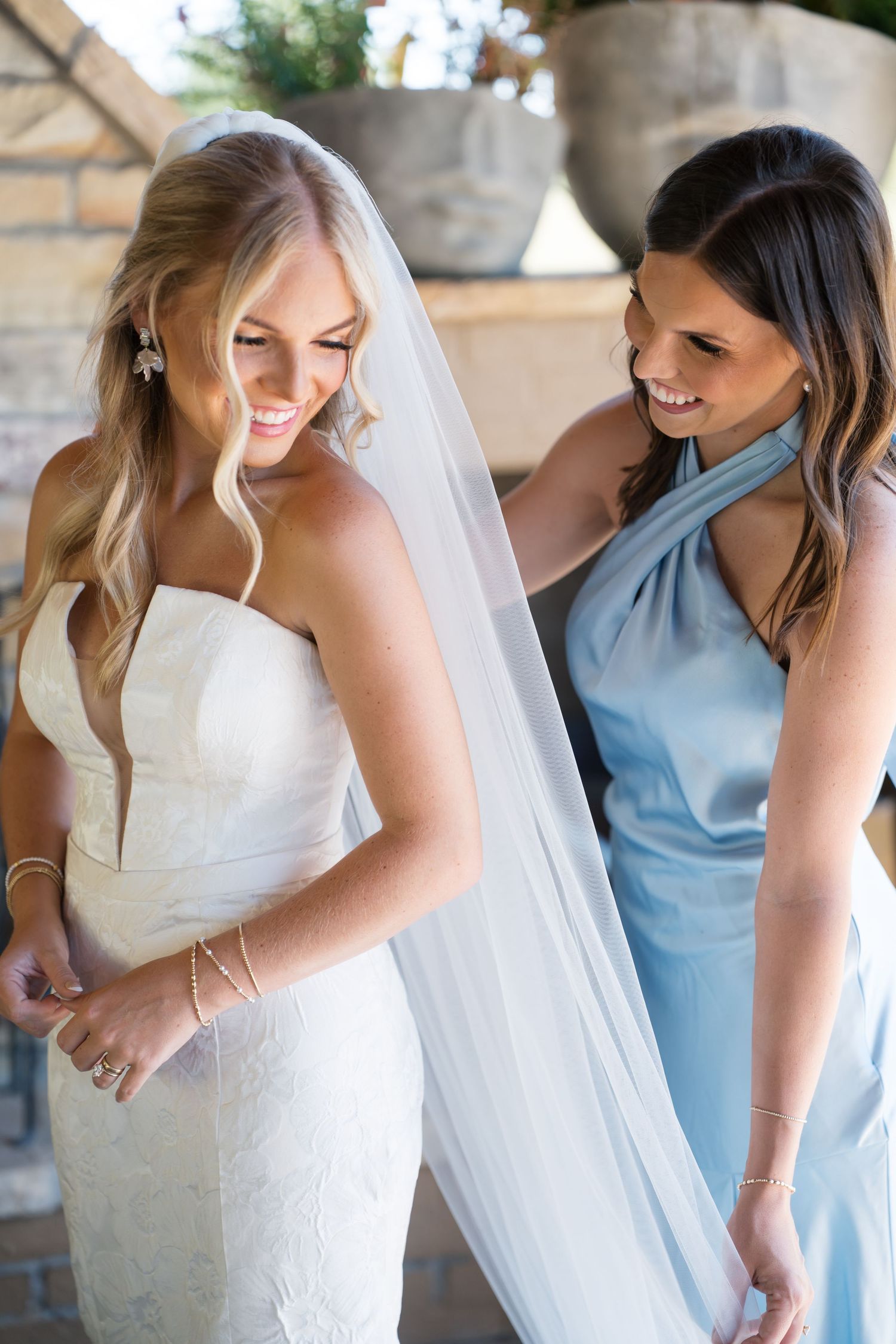 Bride in white gown and bridesmaid in light blue dress share joyful candid moments during wedding photography session.