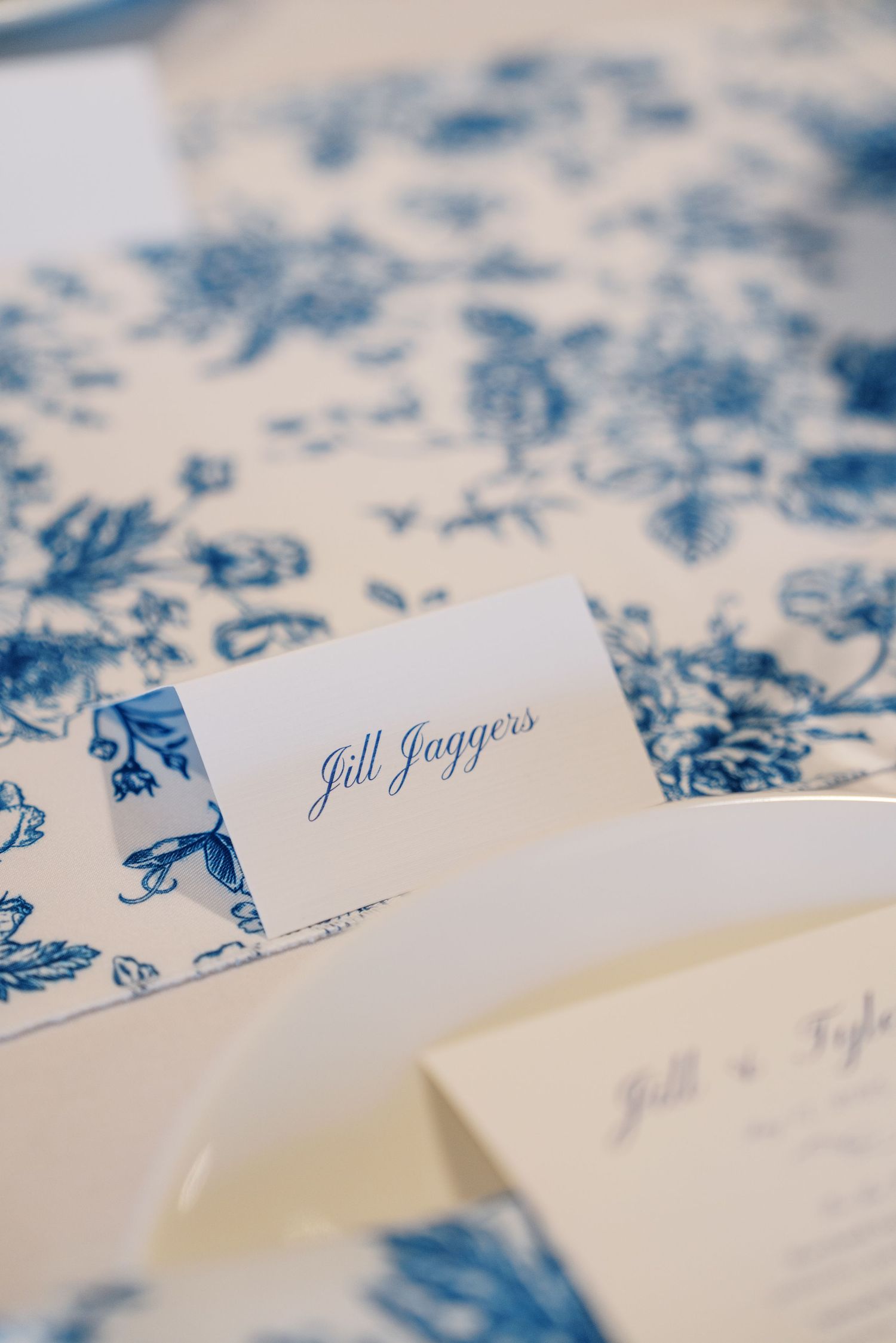 Elegant name card with 'Jill Jaggies' text in blue calligraphy on white paper with floral pattern background.