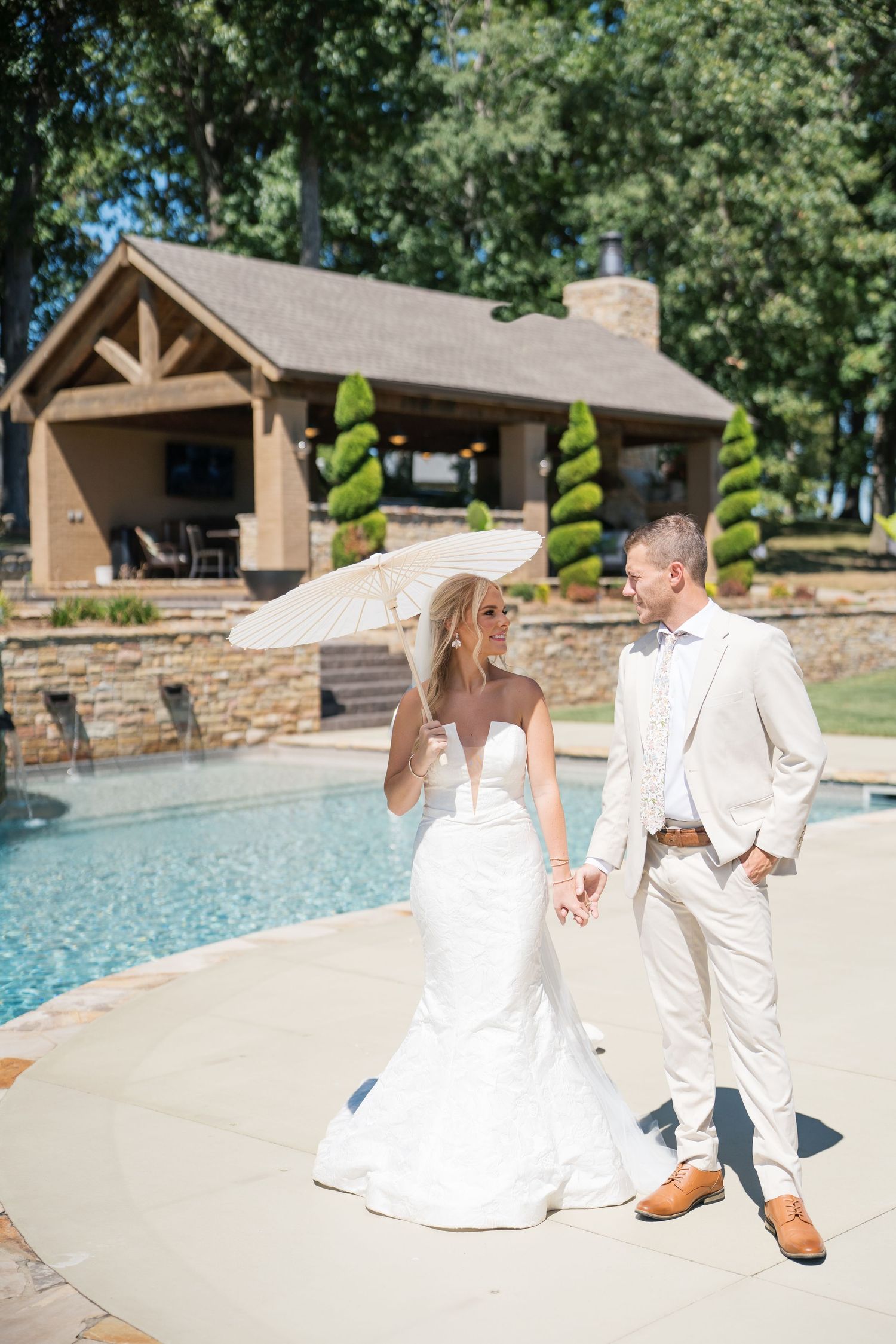 Couple in white attire dancing and twirling gracefully by a swimming pool on a sunny summer day.