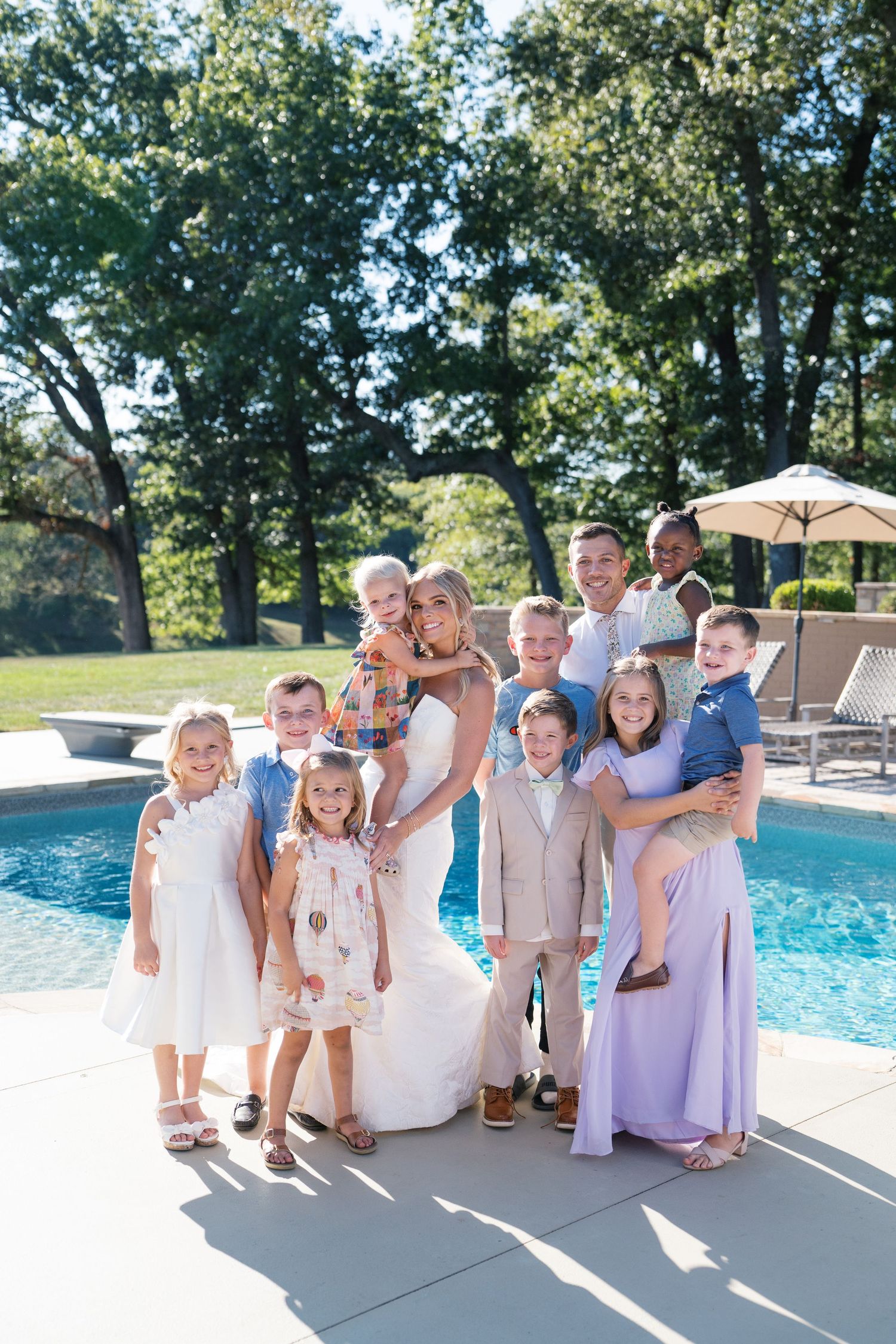 A group poses together on a sunny day by a swimming pool wearing coordinated white and pastel outfits.