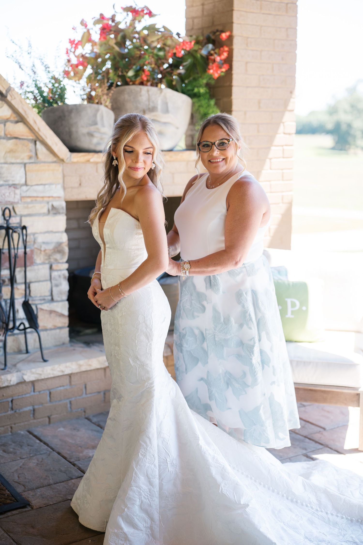 A bride and companion share a joyful moment together on a covered stone patio during a wedding celebration.
