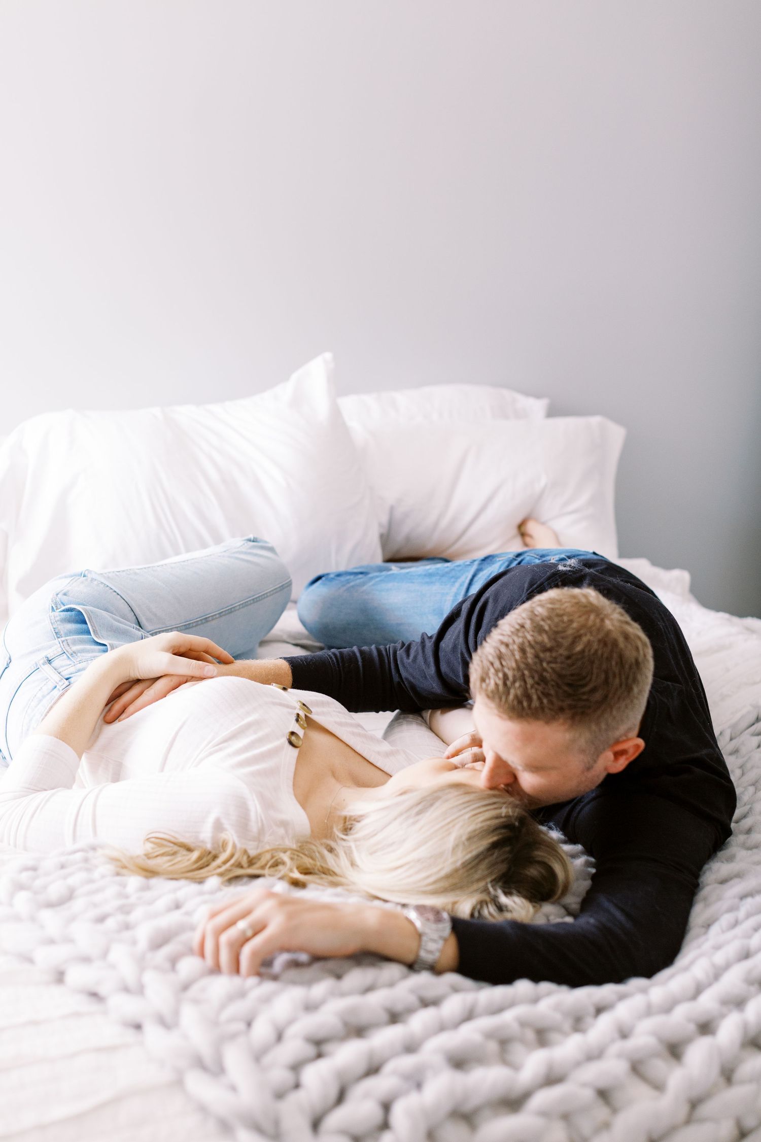 A couple shares an intimate moment while resting together on a white bed with a chunky knit blanket. Nashville Wedding Photographer