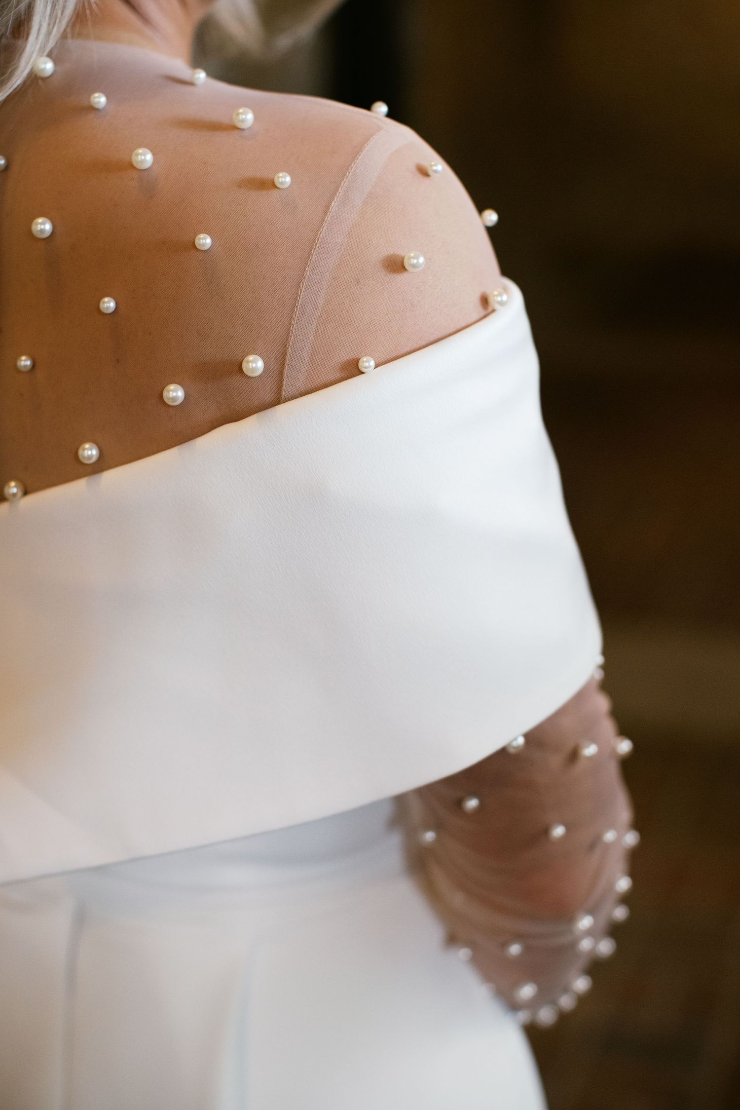 Close-up detail of a sheer wedding dress sleeve adorned with delicate pearl beads and white satin trim.