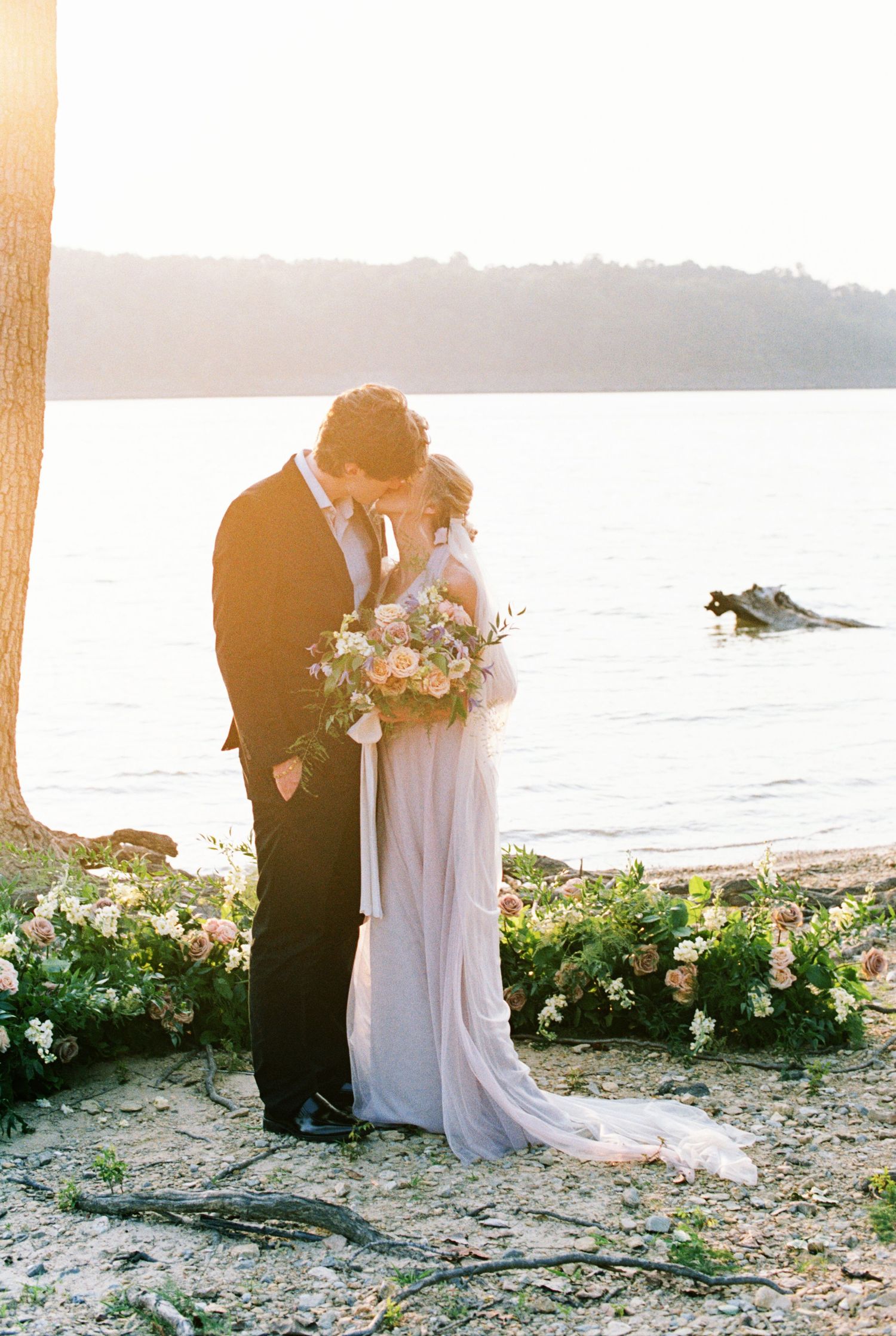 An intimate wedding moment captured by the water with floral decorations at sunset. Kirstie Whitaker Photography