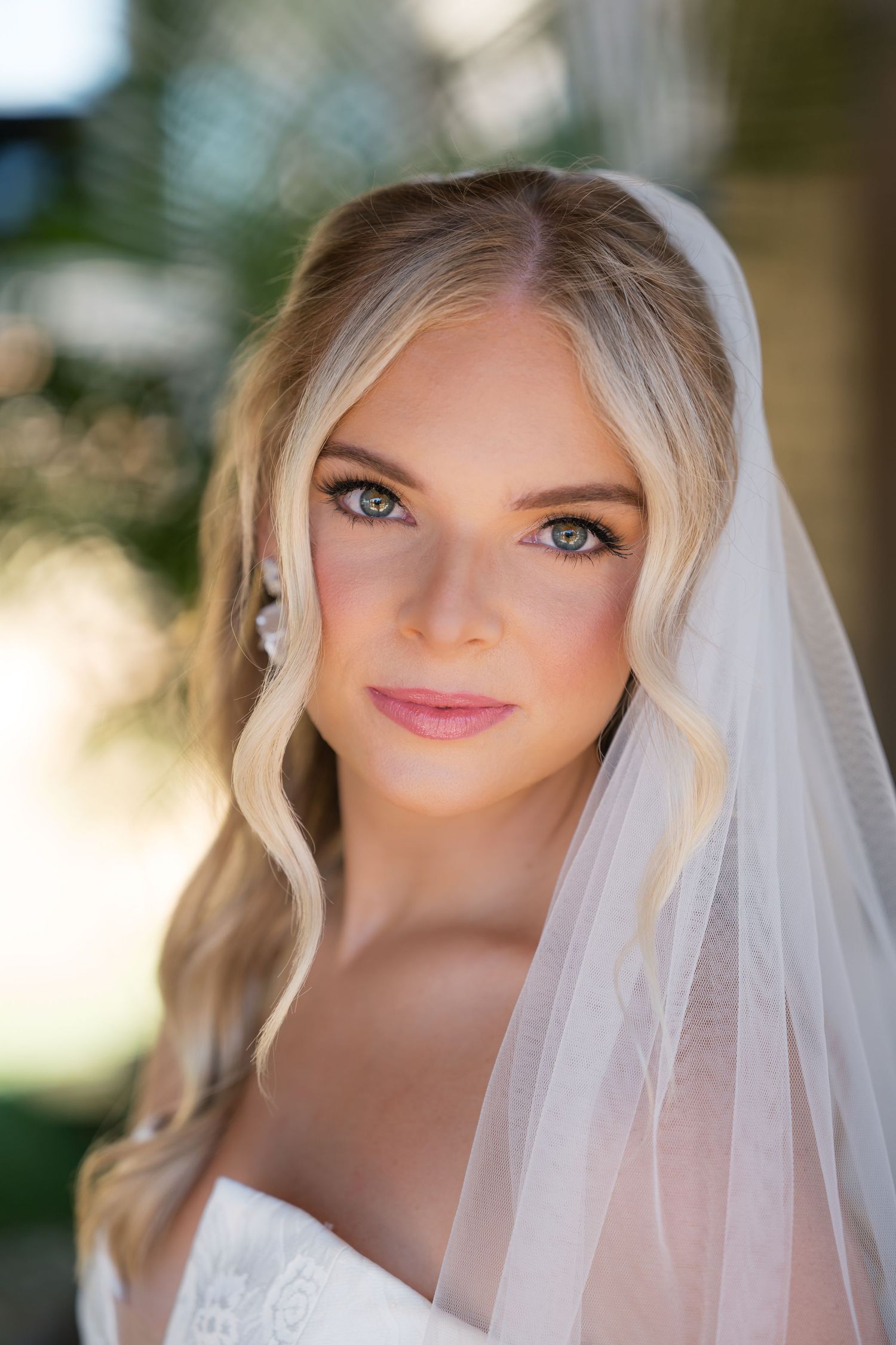 Close up portrait of a bride wearing a delicate white veil and soft makeup in natural lighting.