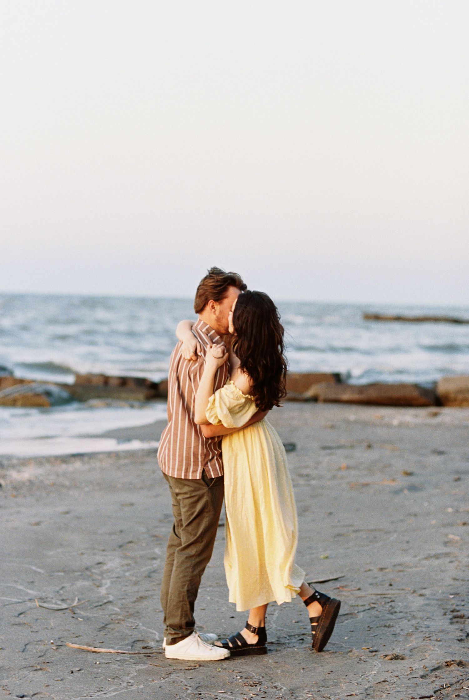 A romantic couple embracing on a beach at sunset with ocean waves in the background.
