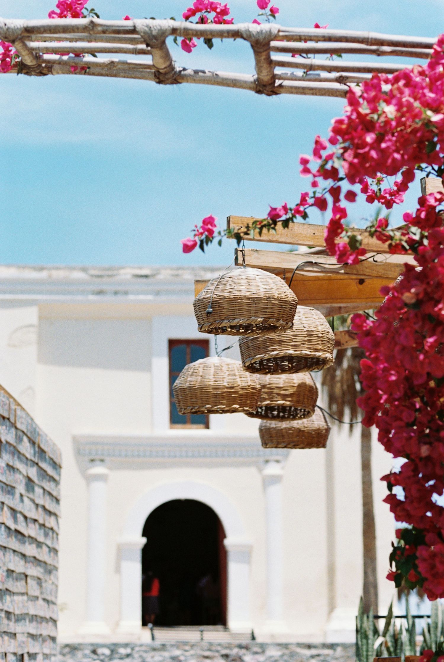 Mediterranean archway adorned with bright pink bougainvillea and hanging woven basket lamps. Kirstie Whitaker Photography
