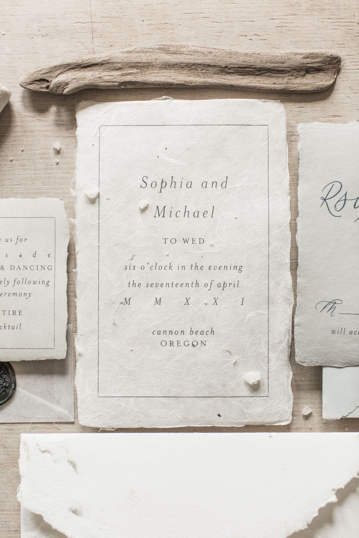 Elegant vintage-style wedding invitation printed in light gray text on textured white paper with driftwood background. Kirstie Whitaker
