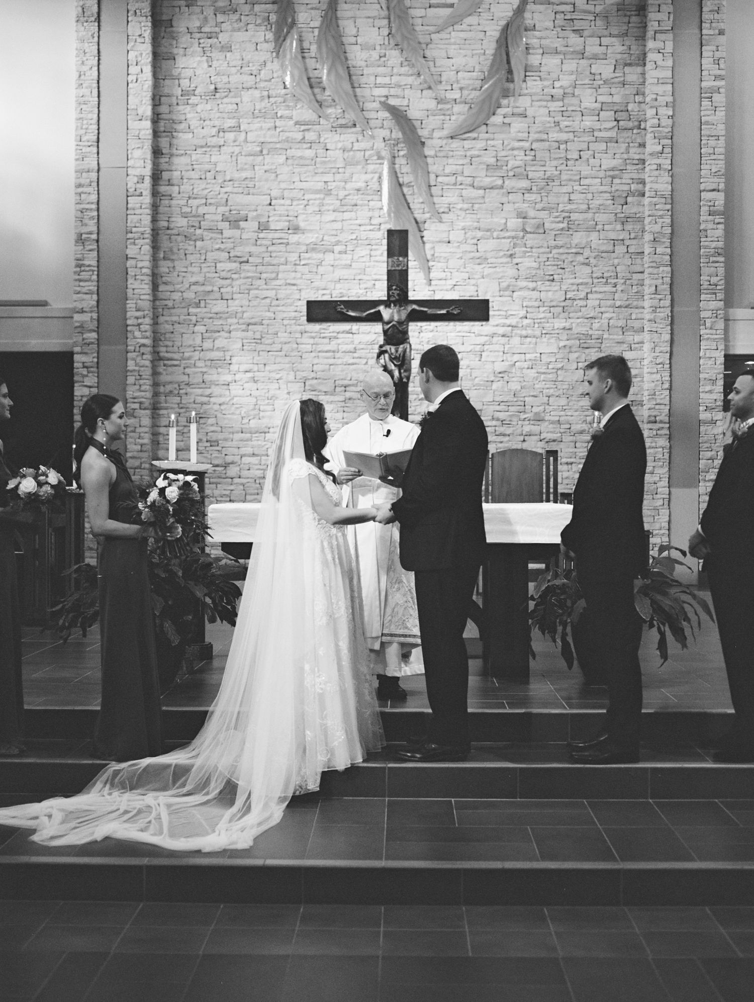 Black and white photo of wedding ceremony in church with cross and brick wall. Kirstie Whitaker Photography