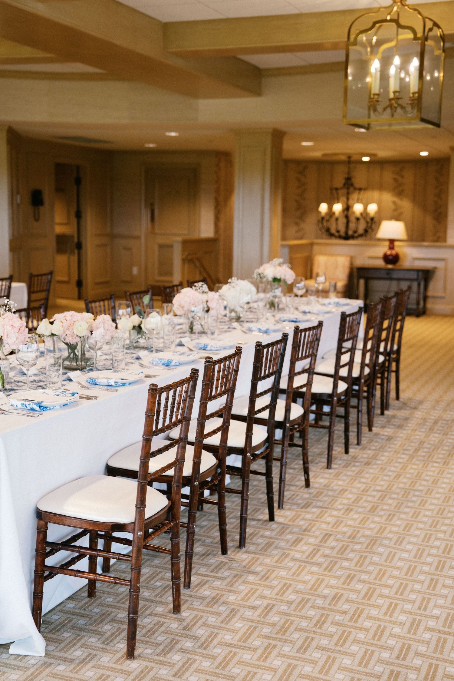 Elegant dining table setup with dark wooden Chiavari chairs and white linens under brass lantern in upscale banquet room.