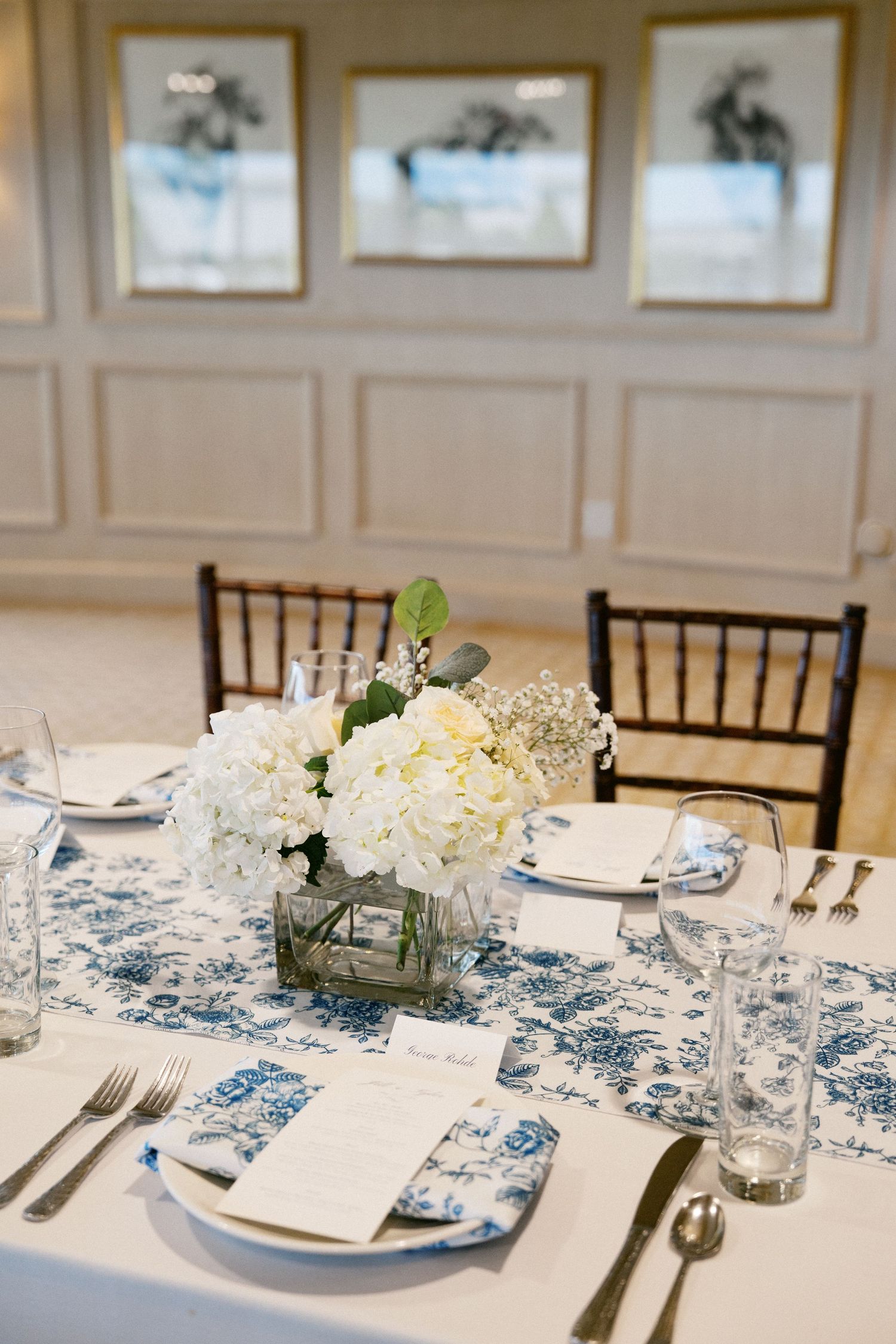Elegant table setting with white hydrangeas centerpiece and blue toile pattern runner at formal event.