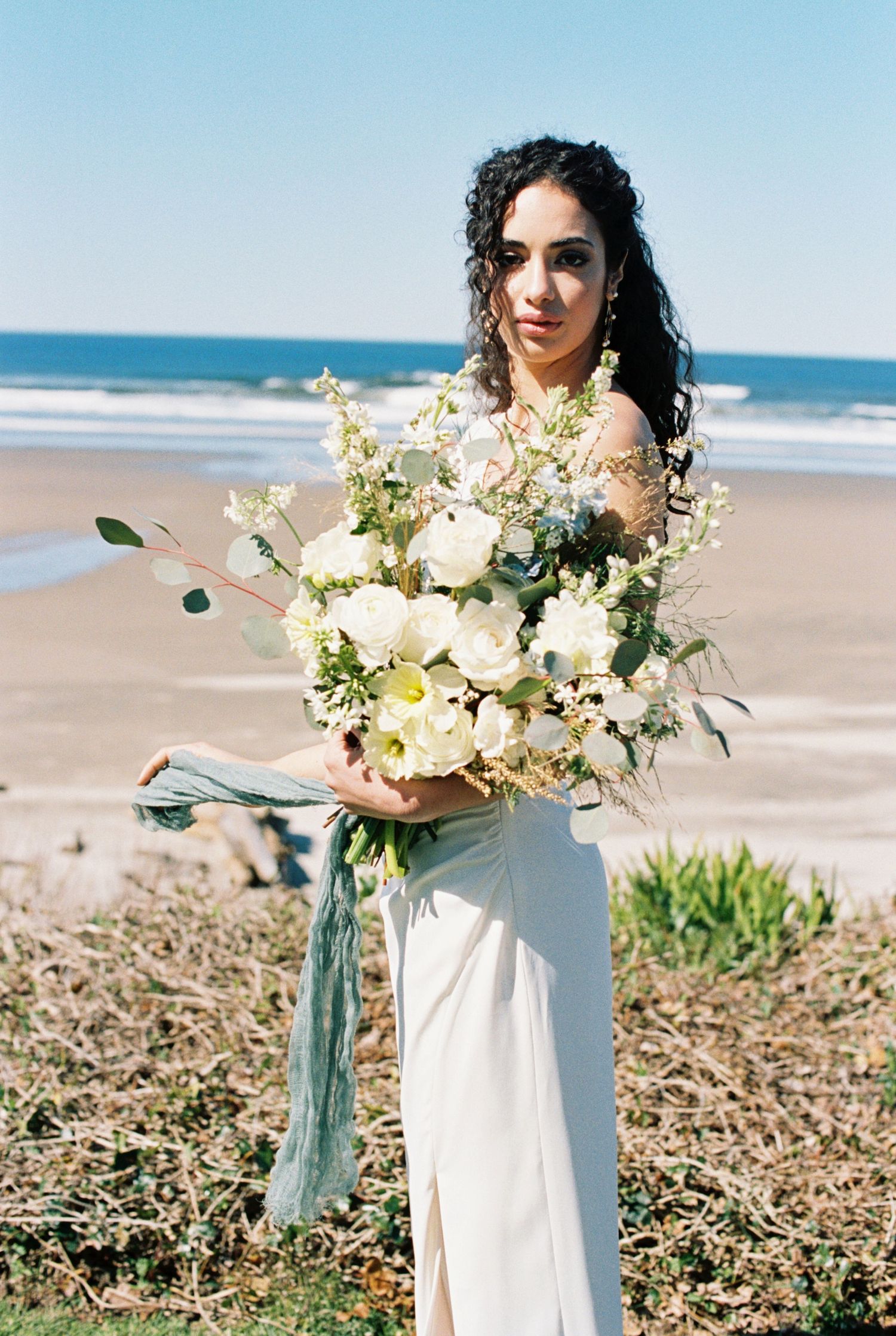 A stunning beach wedding scene with a beautiful white and cream floral bouquet held against a pristine oceanfront backdrop.