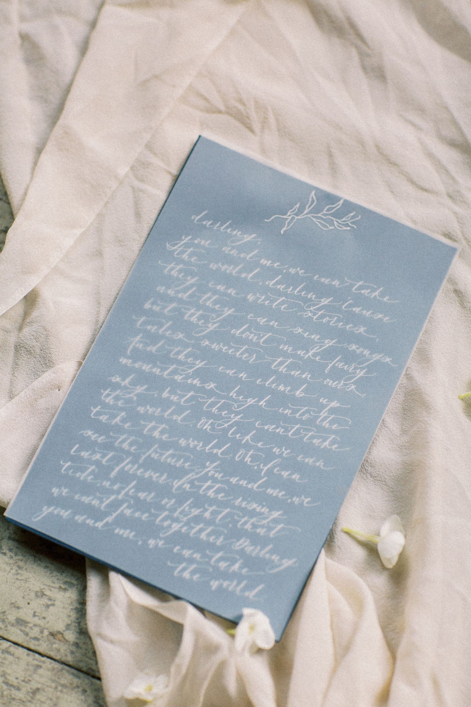 A blue wedding invitation with elegant white calligraphy handwriting on textured fabric background. Kirstie Whitaker Photography