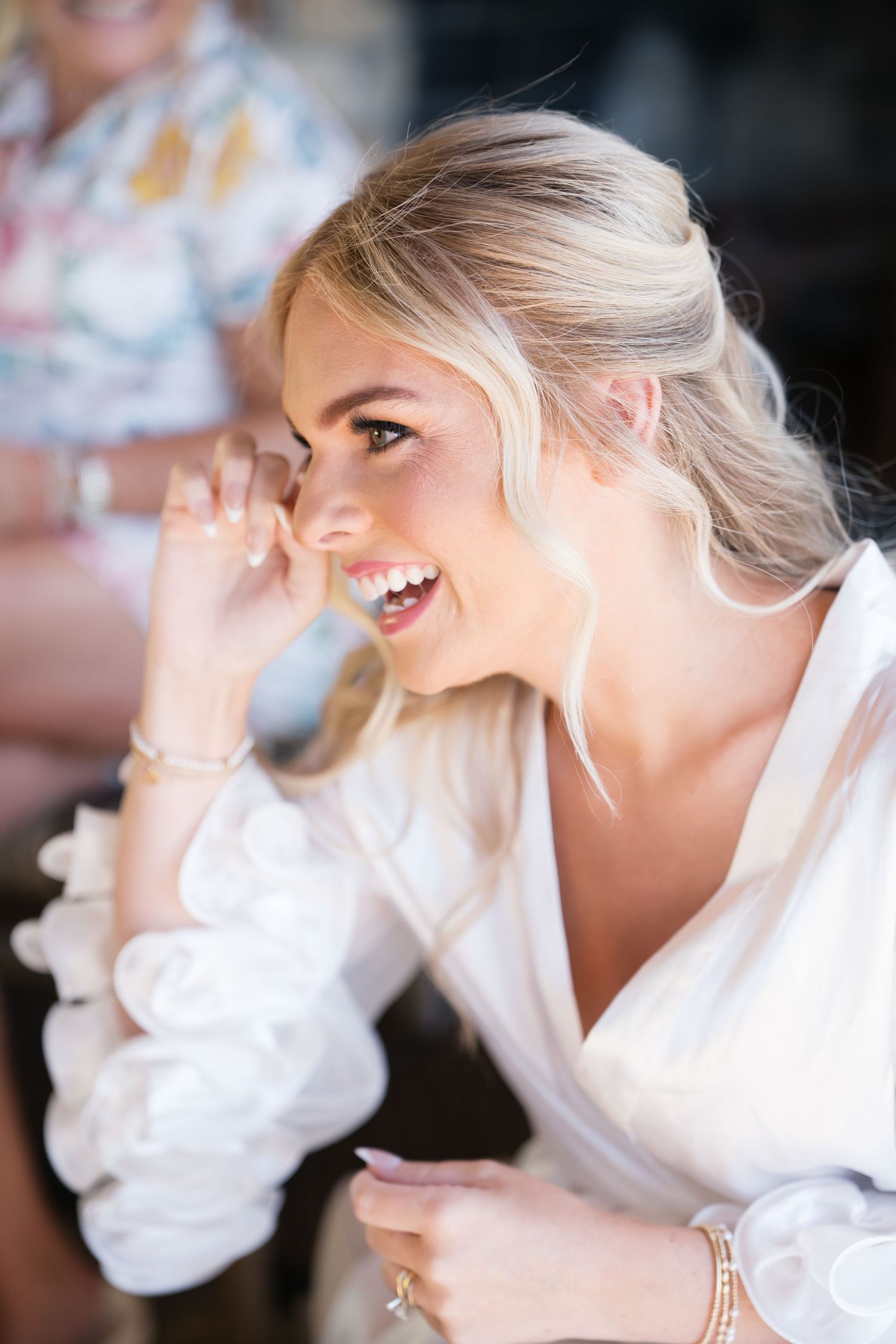 A radiant smile captured in profile during wedding day preparations, wearing a white silk robe with puffy sleeves.