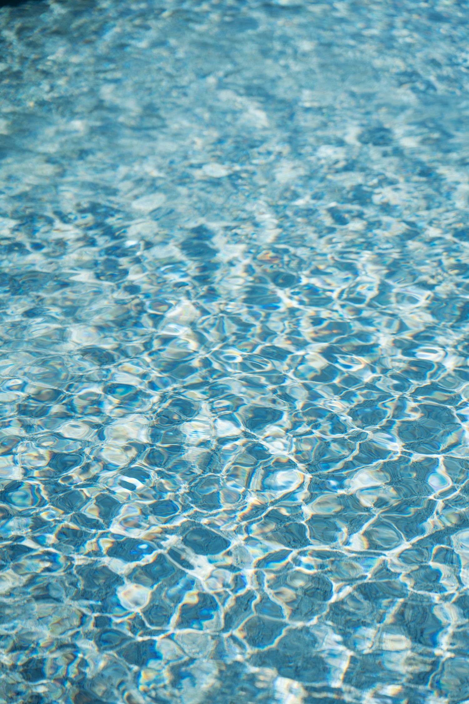 Sunlight creates rippling patterns on crystal clear blue swimming pool water with a mesmerizing reflective surface.