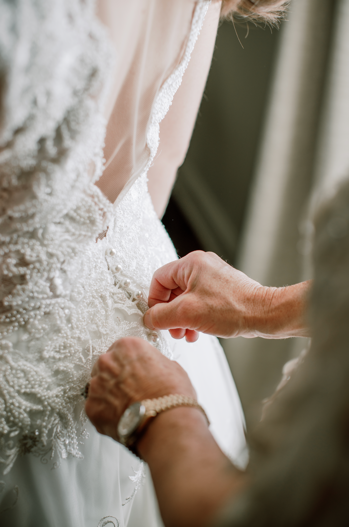 Hands carefully adjusting delicate white lace details on an elegant wedding dress.
