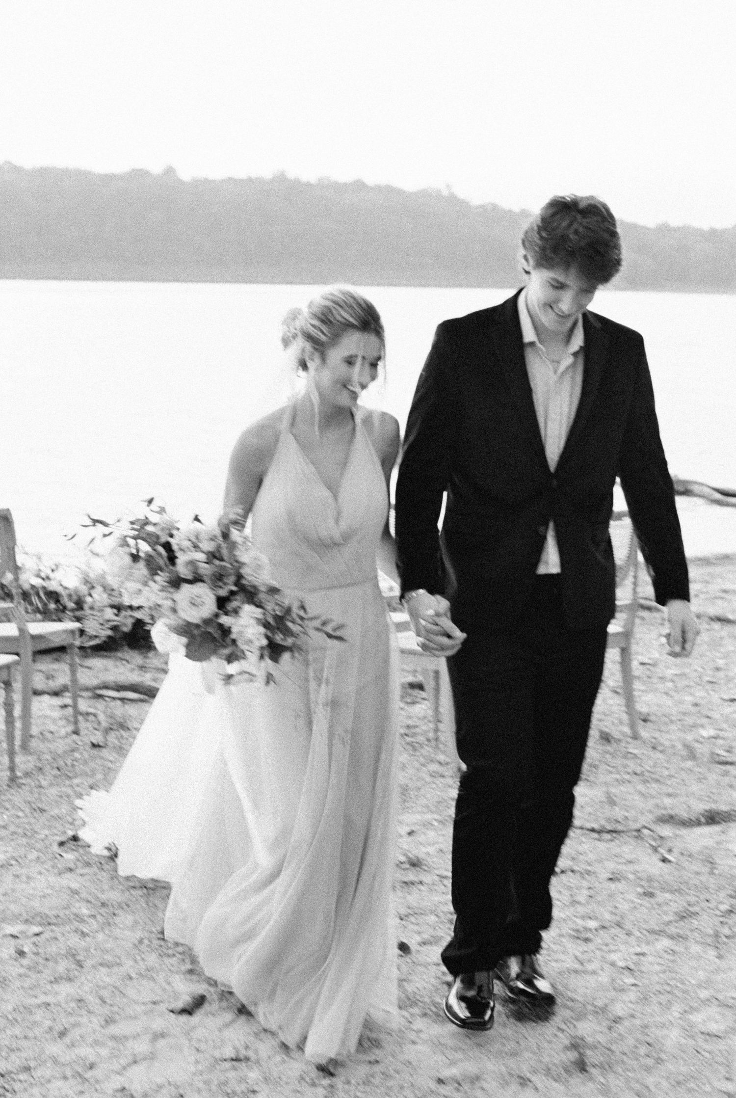 A couple walks together on a beach during their wedding day, with the bride holding a bouquet in a flowing white dress.
