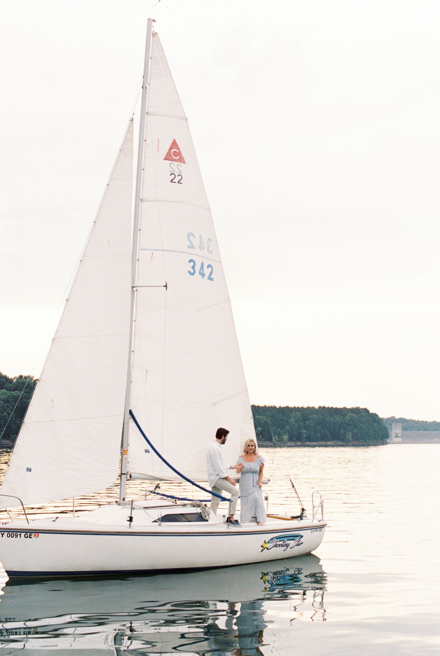 White sailboat with triangular sail shown in calm waters during serene evening light.