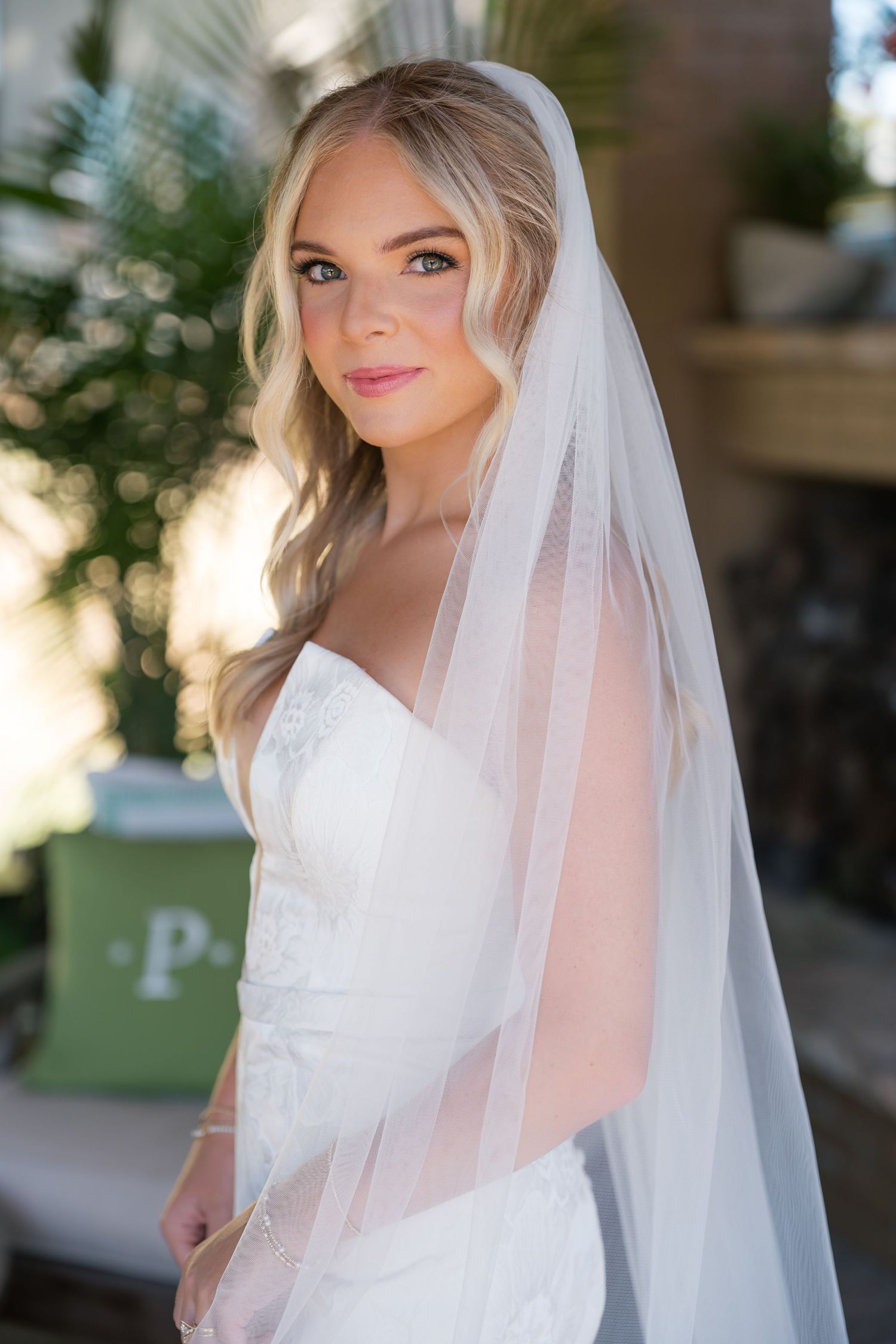 A bride in a white lace wedding dress and flowing veil poses for a series of elegant bridal portraits outdoors.