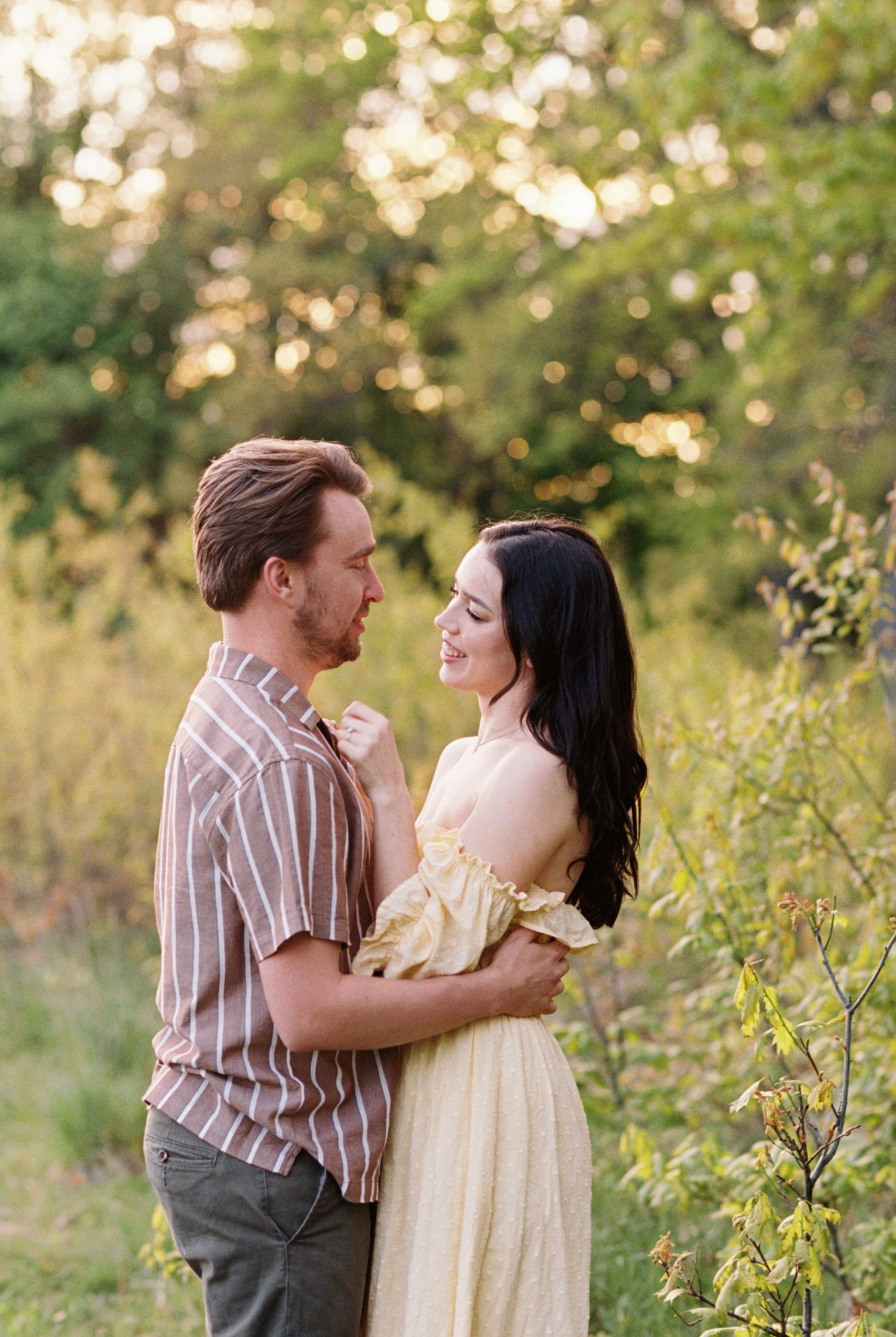 Romantic couple embraces in a sun-dappled garden setting during golden hour while wearing vintage-inspired clothing.