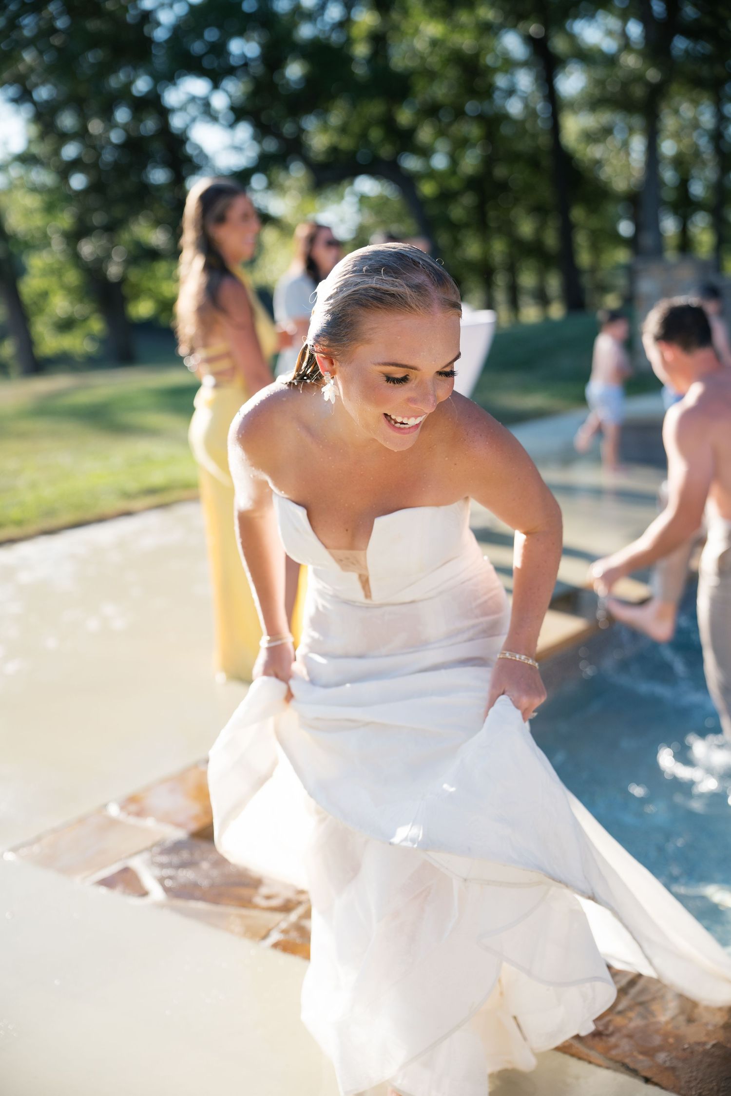 A bride in a white strapless wedding dress smiles while dancing outdoors on a sunny summer day.