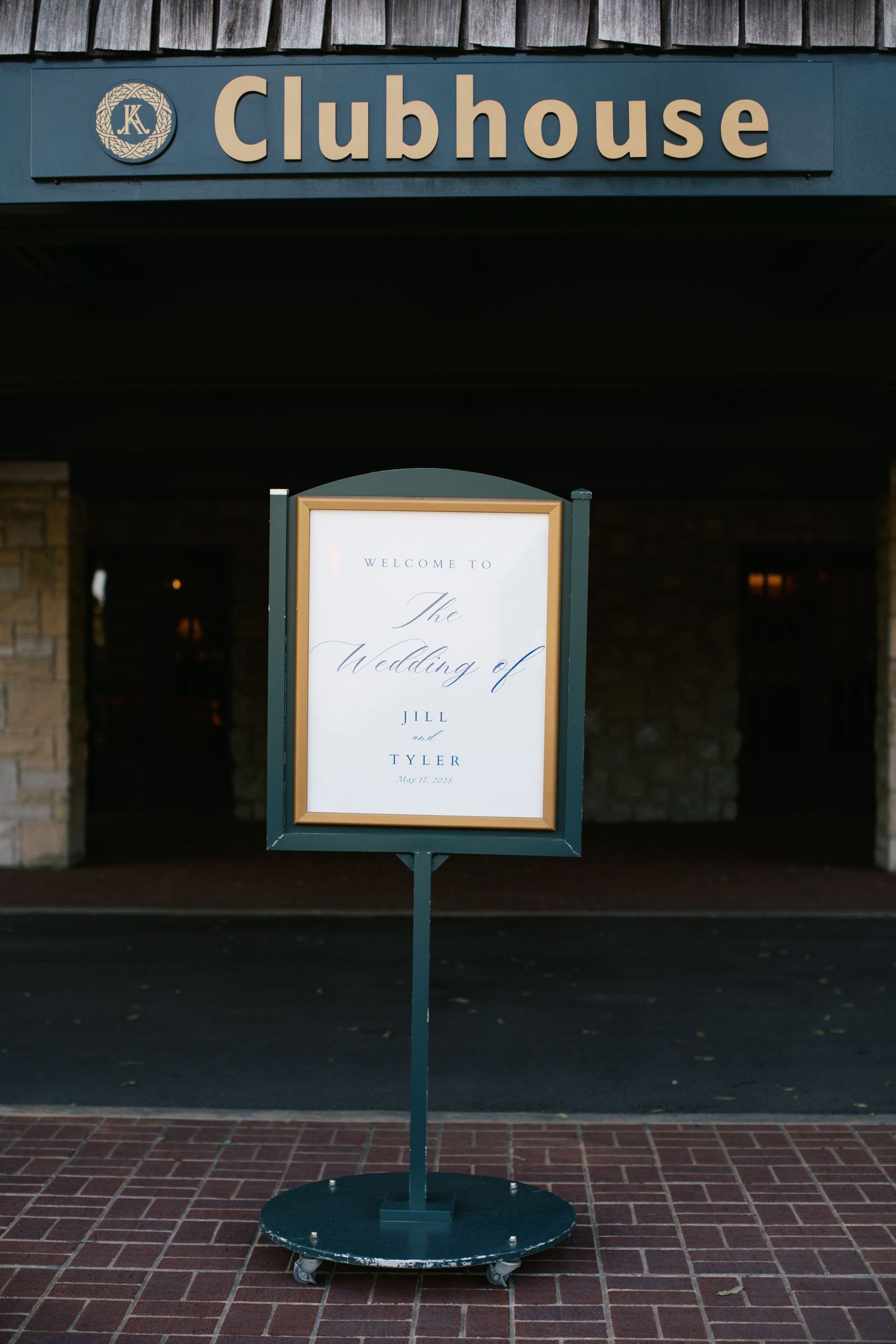 A green-tinted clubhouse entrance sign and standing menu board on brick pavement outside a dark building.