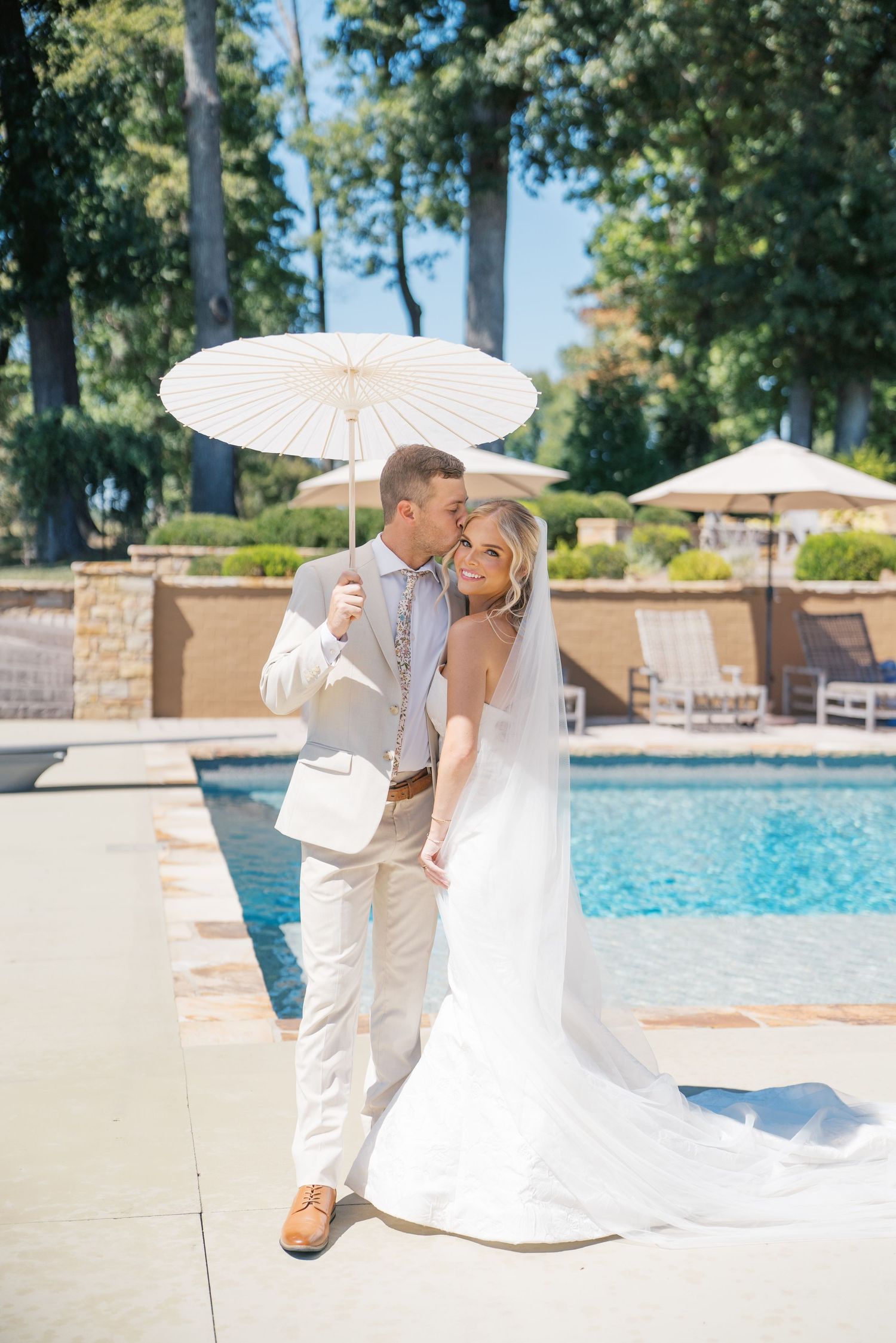 Elegant couple shares romantic moment by pool with white parasol on sunny summer day at luxury resort.