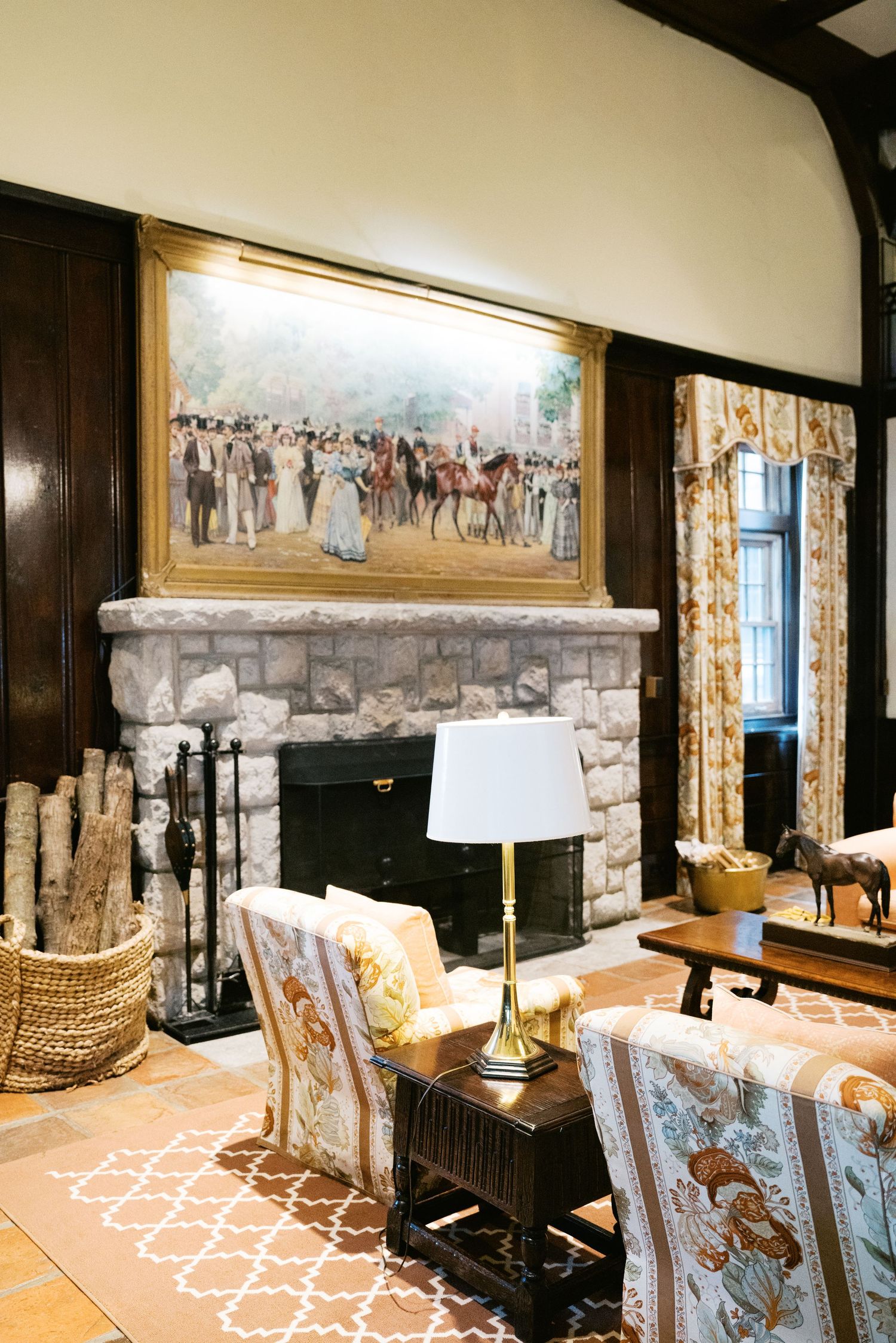 Elegant living room with stone fireplace, vintage artwork, upholstered chairs and patterned rug in classic home decor style.