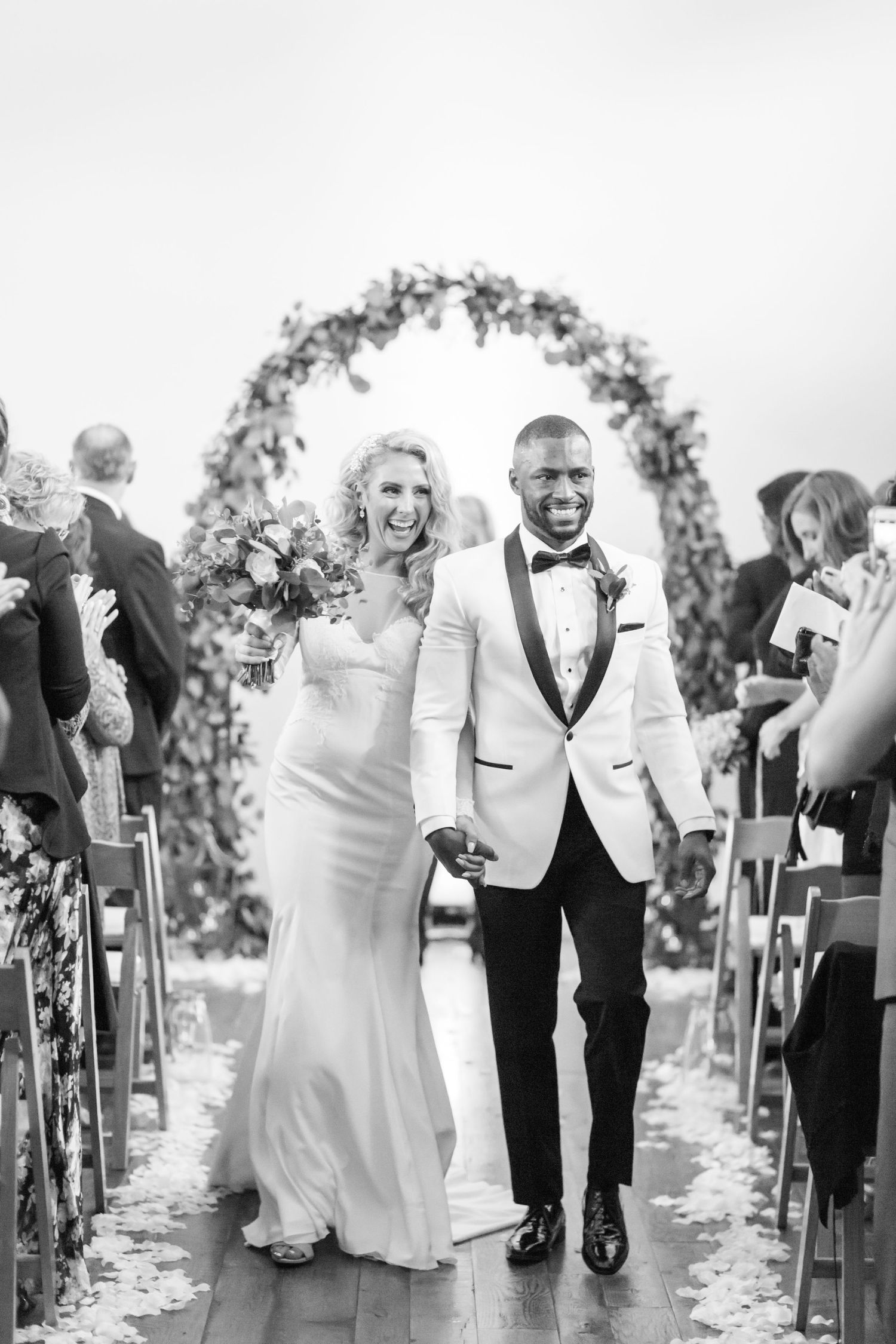 A joyful newlywed couple walks down the aisle together under a floral arch after their wedding ceremony.